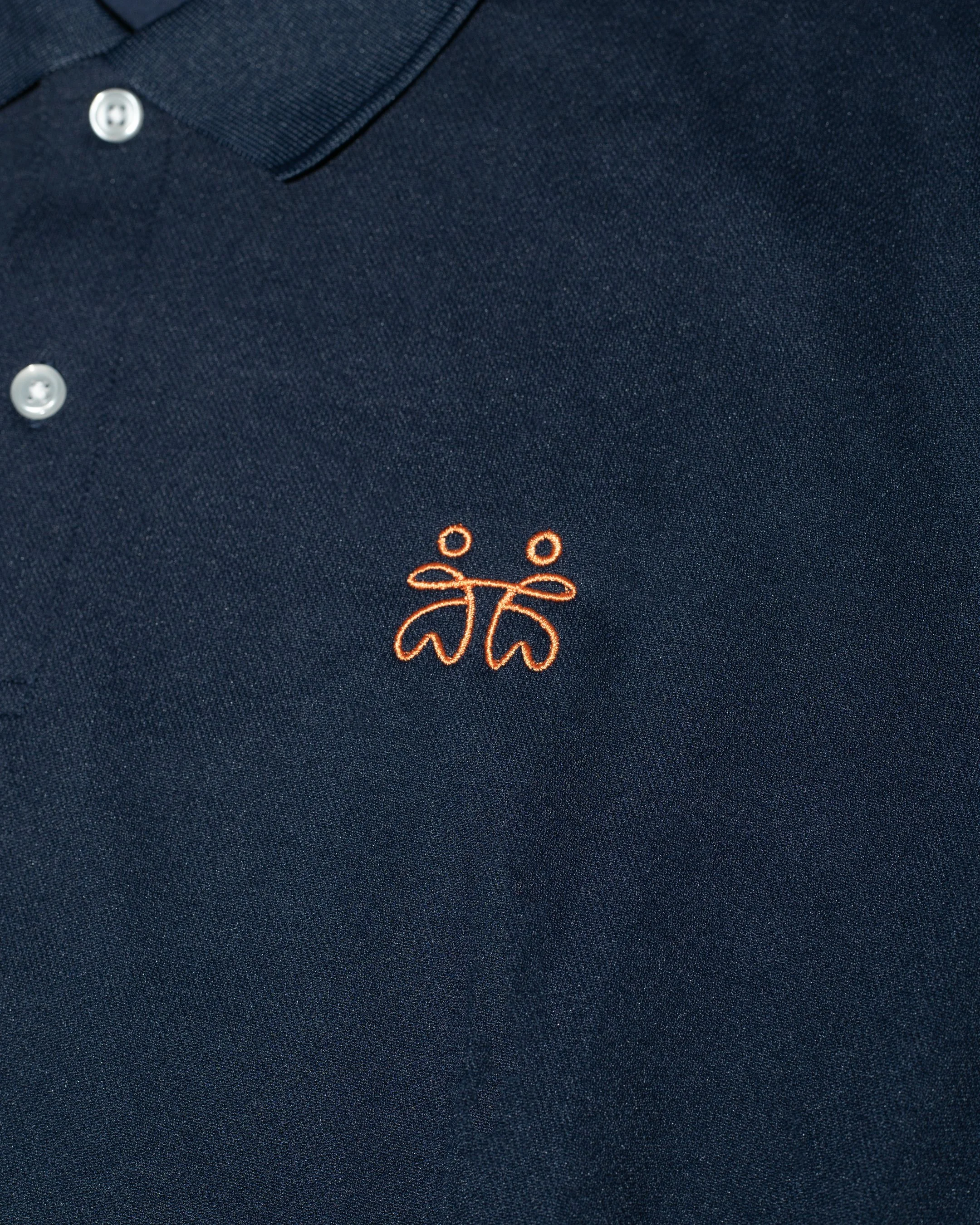 Close-up of a dark navy polo shirt with white buttons, orange embroidered logo of scissors and thread near the bottom center.