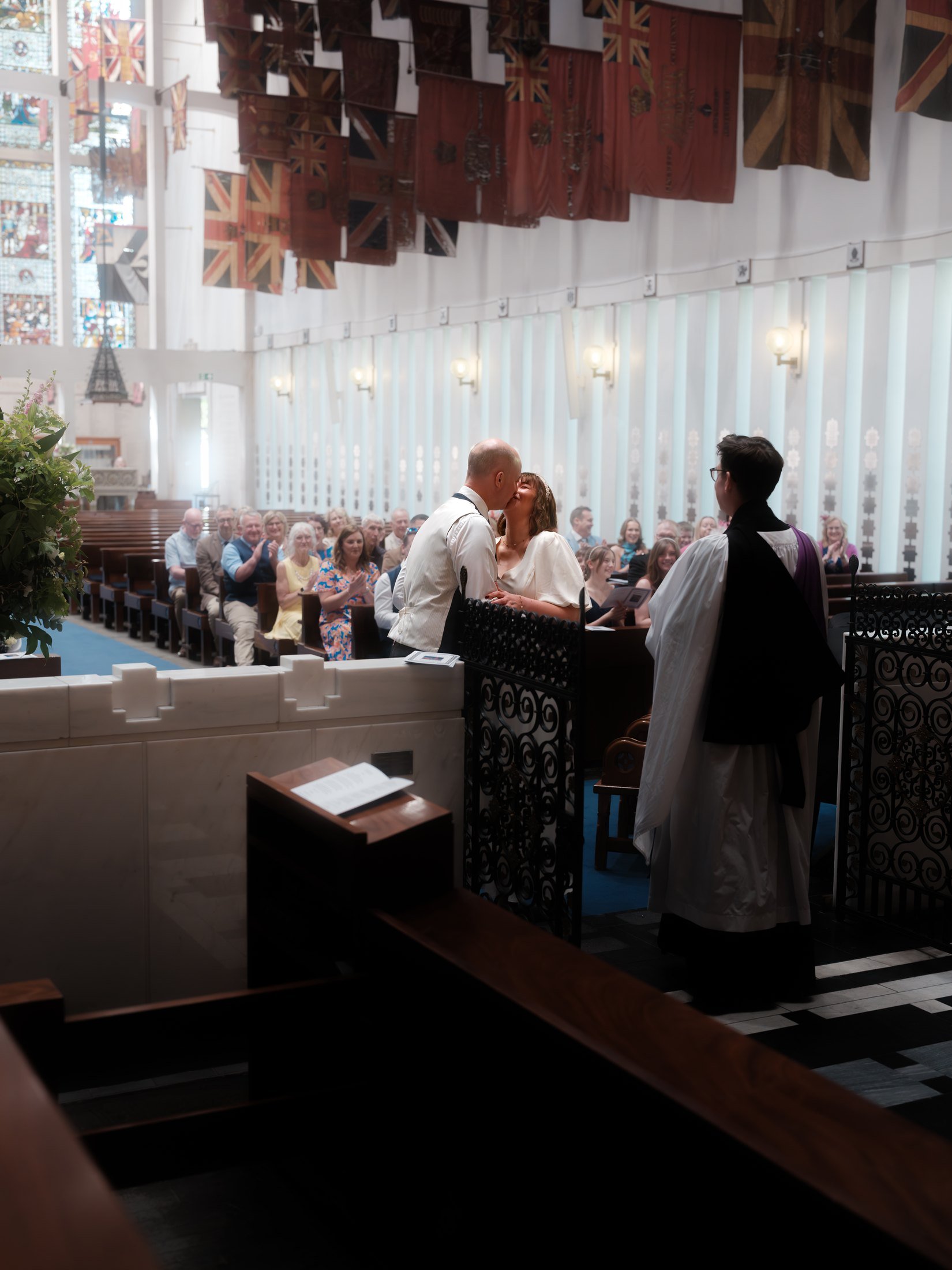 A couple stand together before the altar in a chapel hung with flags.