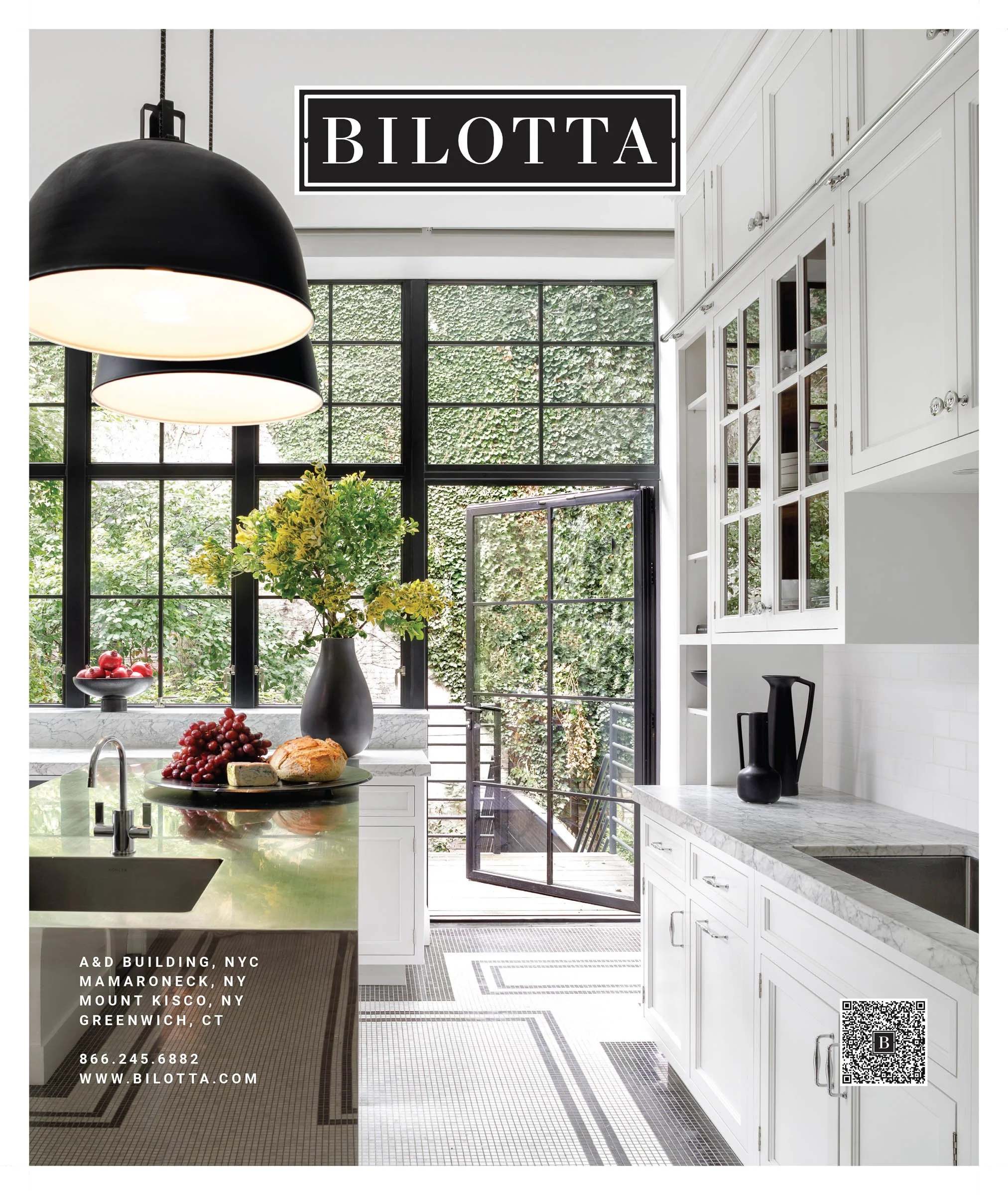 Elegant kitchen advertisement for Bilotta, showcasing a modern design with white cabinetry, marble countertops, black pendant lighting, and a view through large windows. A platter with bread and grapes is on the countertop. The contact information fo
