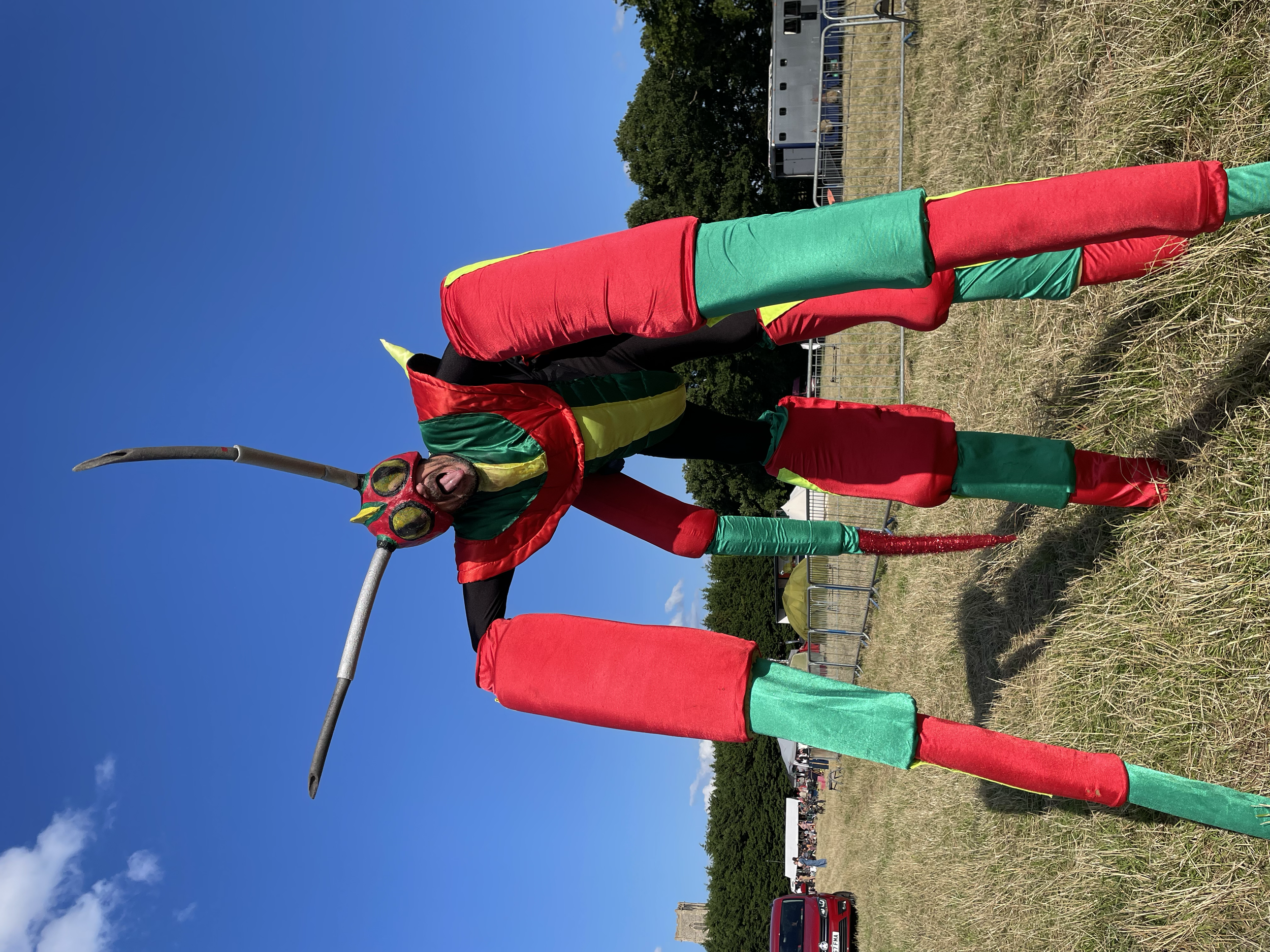 Person dressed up as a giant red and green spider, on very long legs.