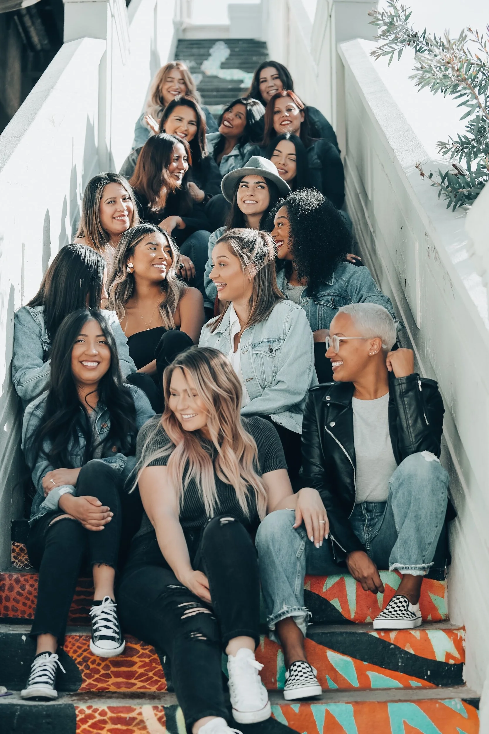 Group of diverse women sitting on colorful stairs, smiling and talking, dressed casually.
