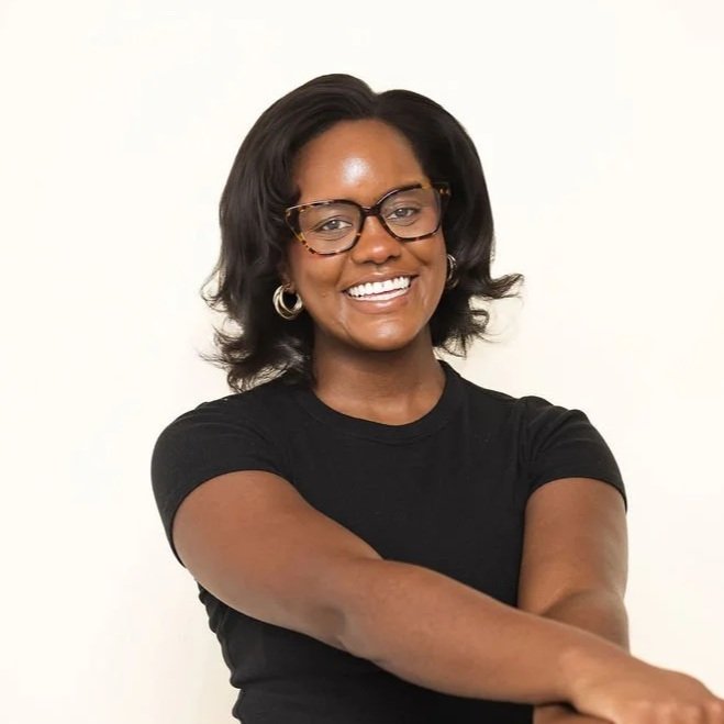 A smiling woman with glasses and hoop earrings in a black shirt posing against a plain white background.