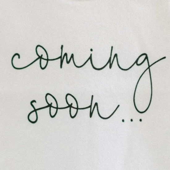 Handwritten phrase 'coming soon...' on white paper in green ink.