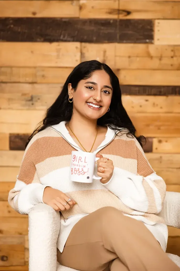 Sanjana Iyer holding a "Girl freaking boss!" mug and smiling for her headshot in Dallas Texas. Sh