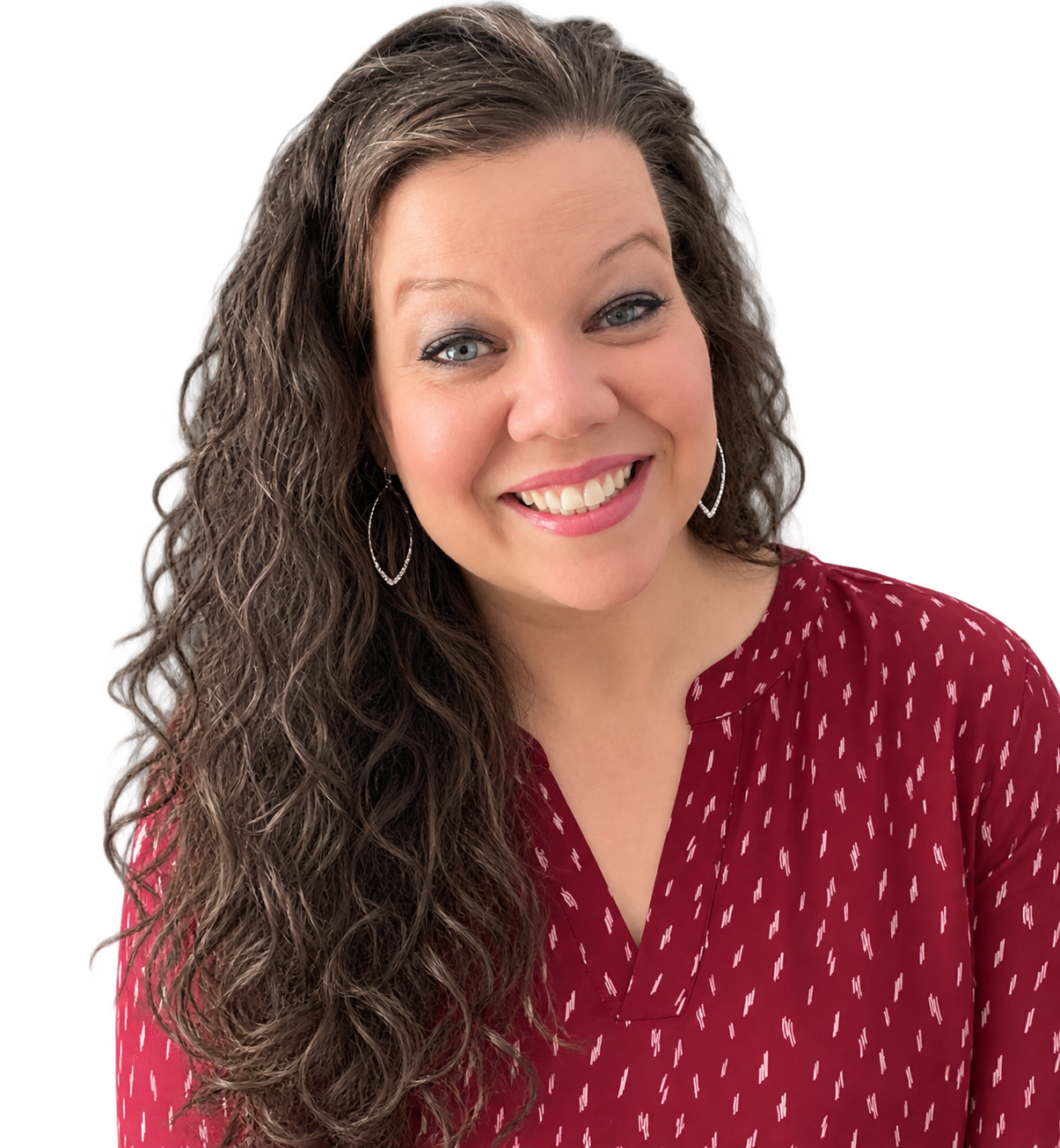 Partial view of a woman with long, curly brown hair smiling, wearing a red dress with white patterns, in front of a bookshelf.