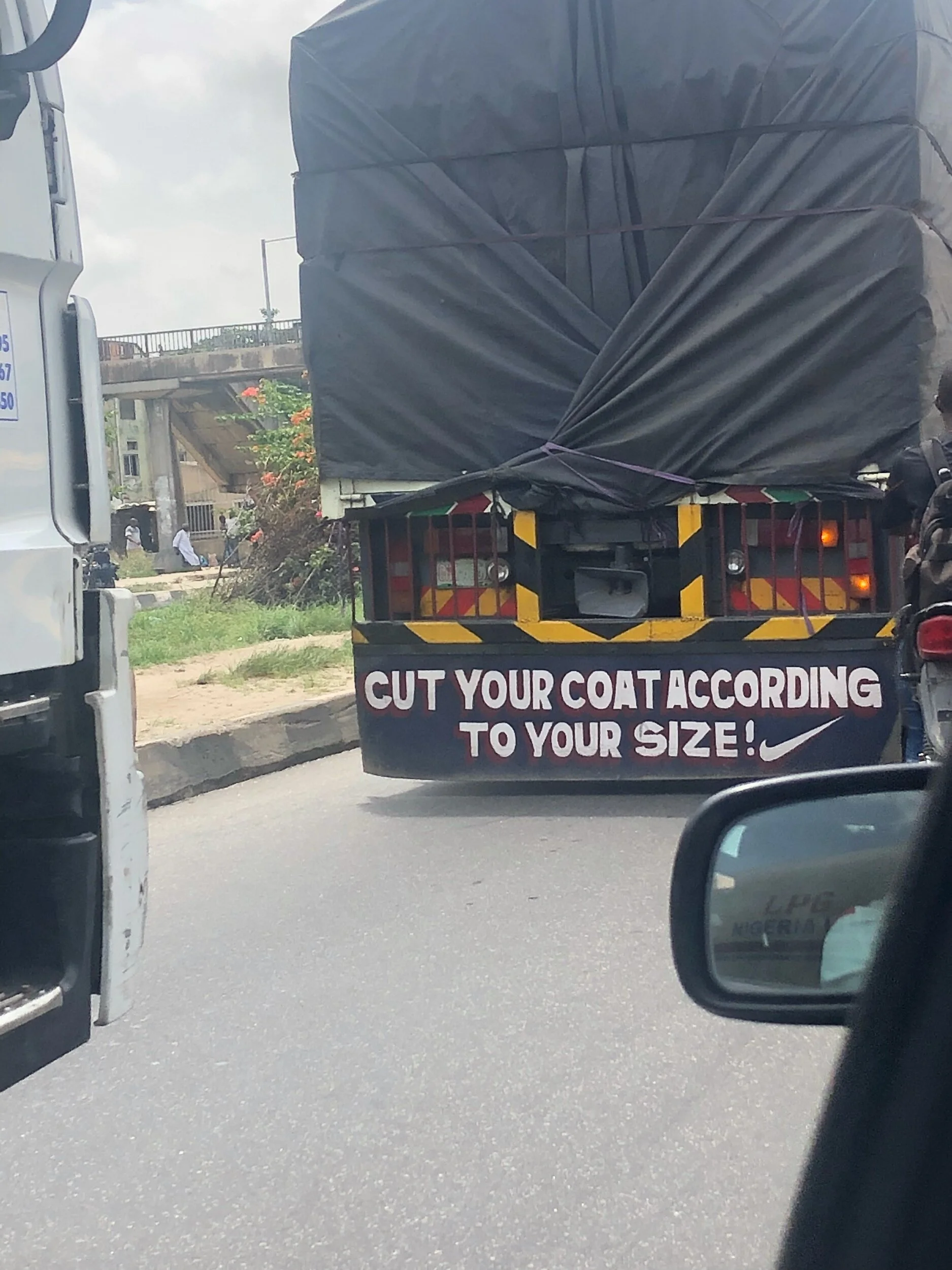 Large truck on the road with a sign that reads, 'CUT YOUR COAT ACCORDING TO YOUR SIZE!'