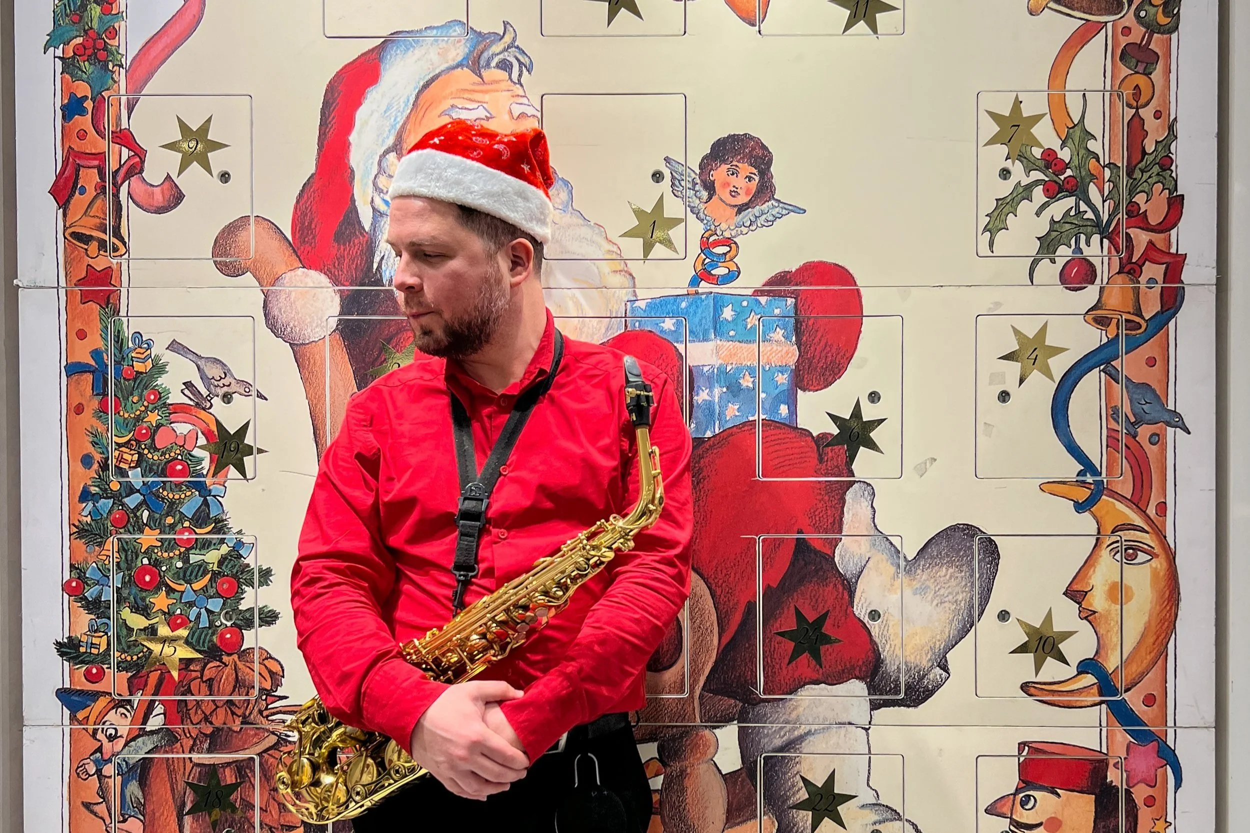 Klim in a Santa hat holding a saxophone, standing in front of a whimsical Christmas-themed backdrop with illustrations of Santa, a Christmas tree, and advent calendar numbers.