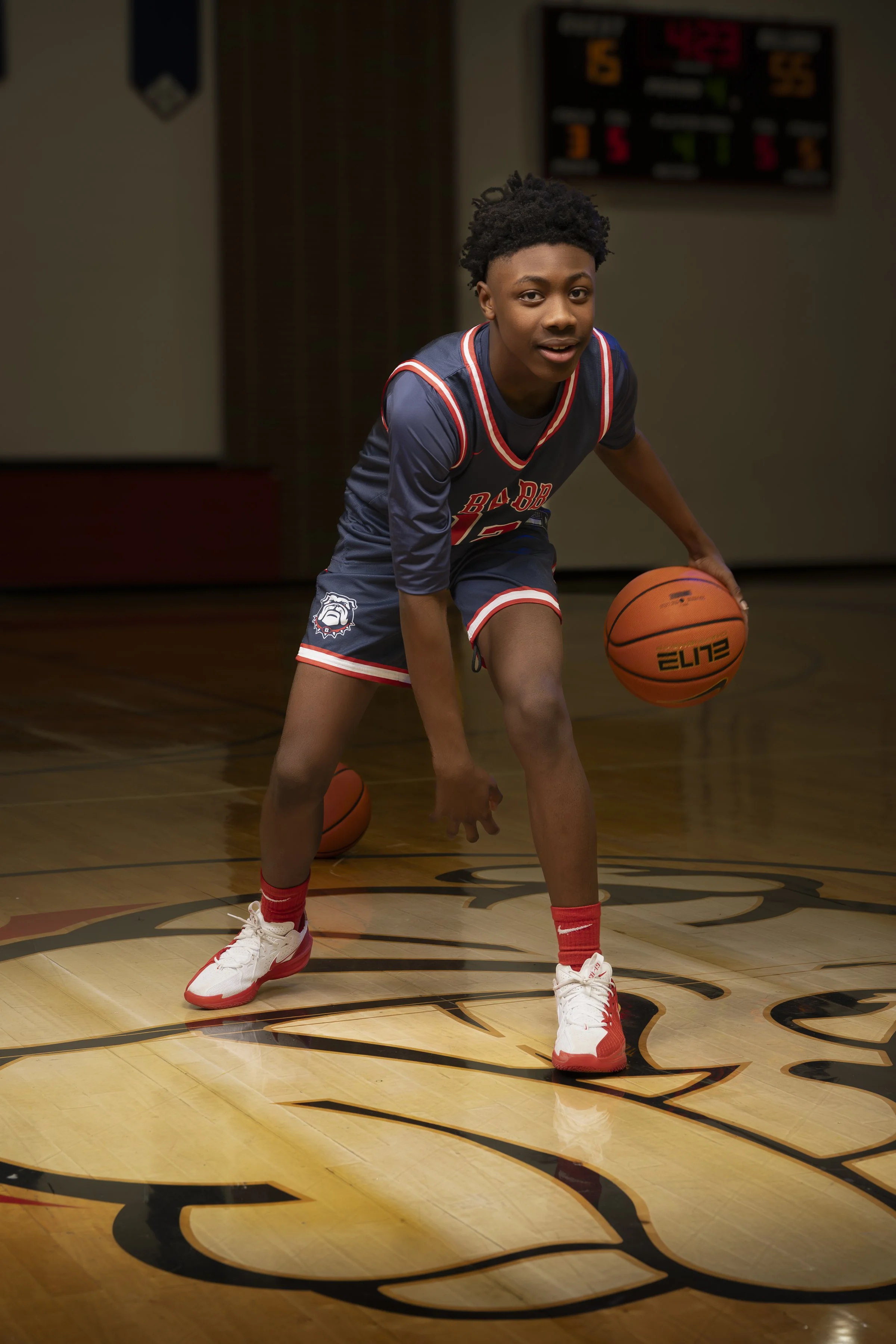 A young basketball player in a navy blue uniform dribbling a basketball on a court.