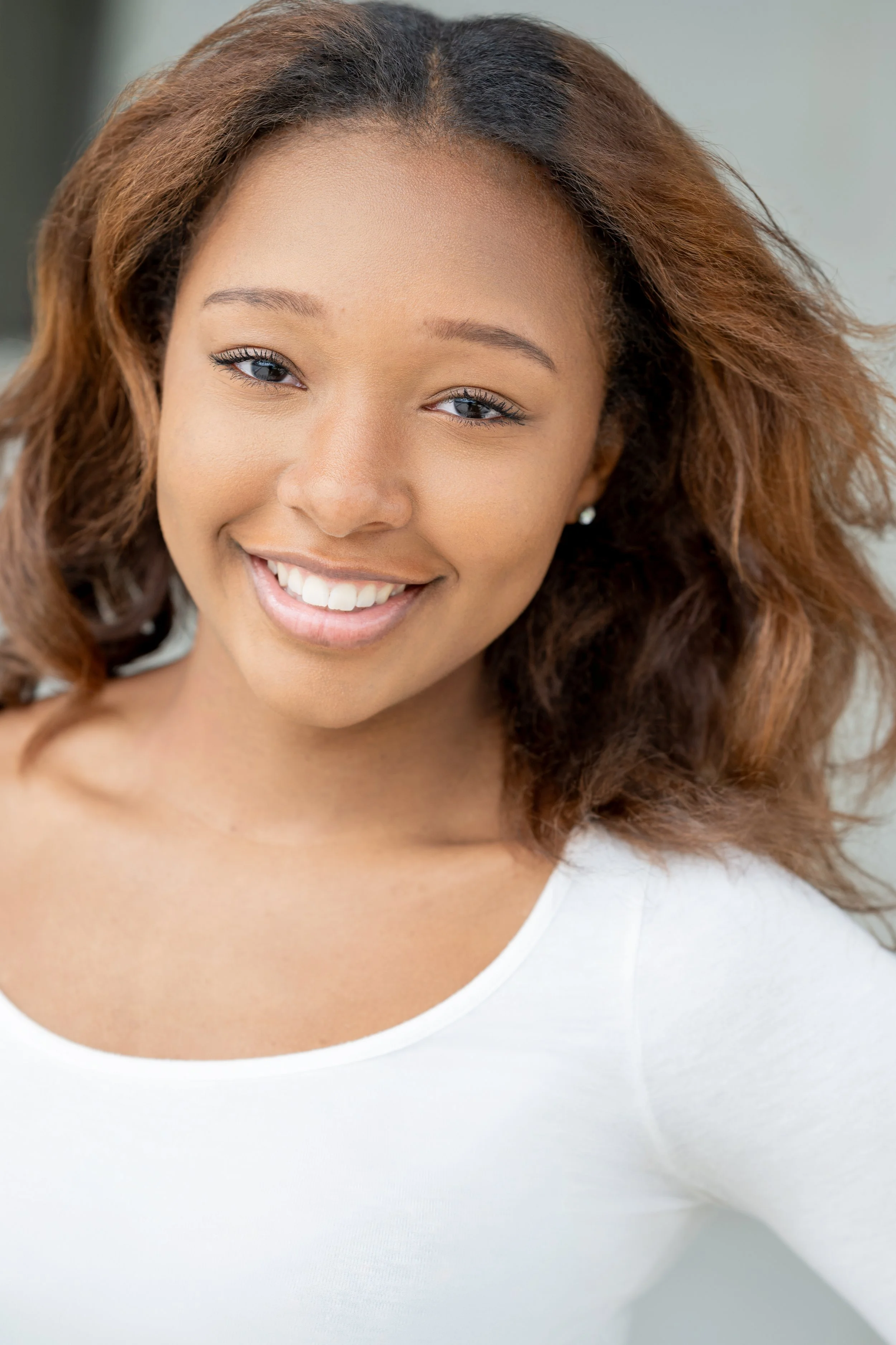 Close-up portrait of a smiling young woman with wavy hair, wearing a white top.