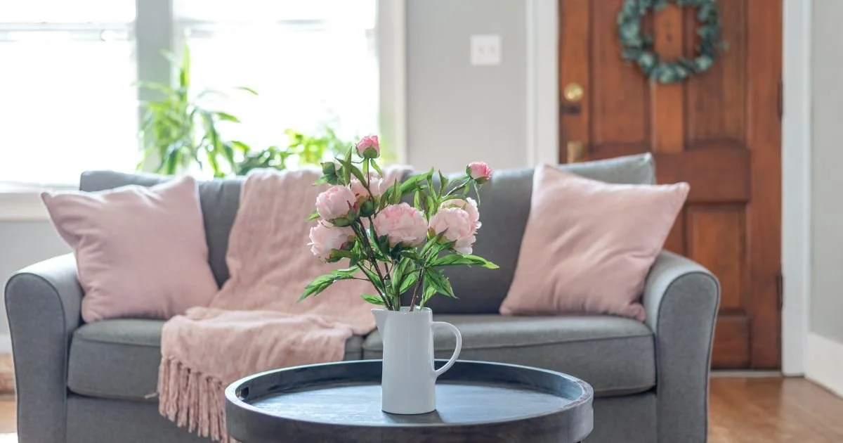 a cozy couch with blankets and pillows and a tale with a vase of flowers