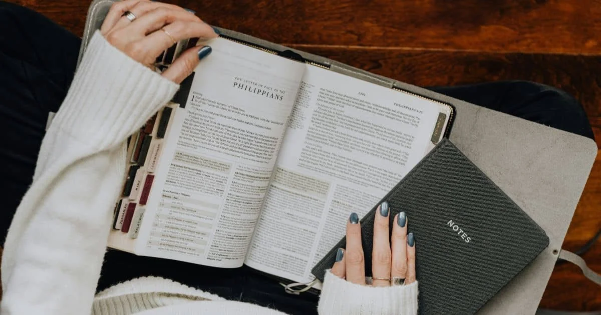 A woman sitting with an open Bible and a journal notebook