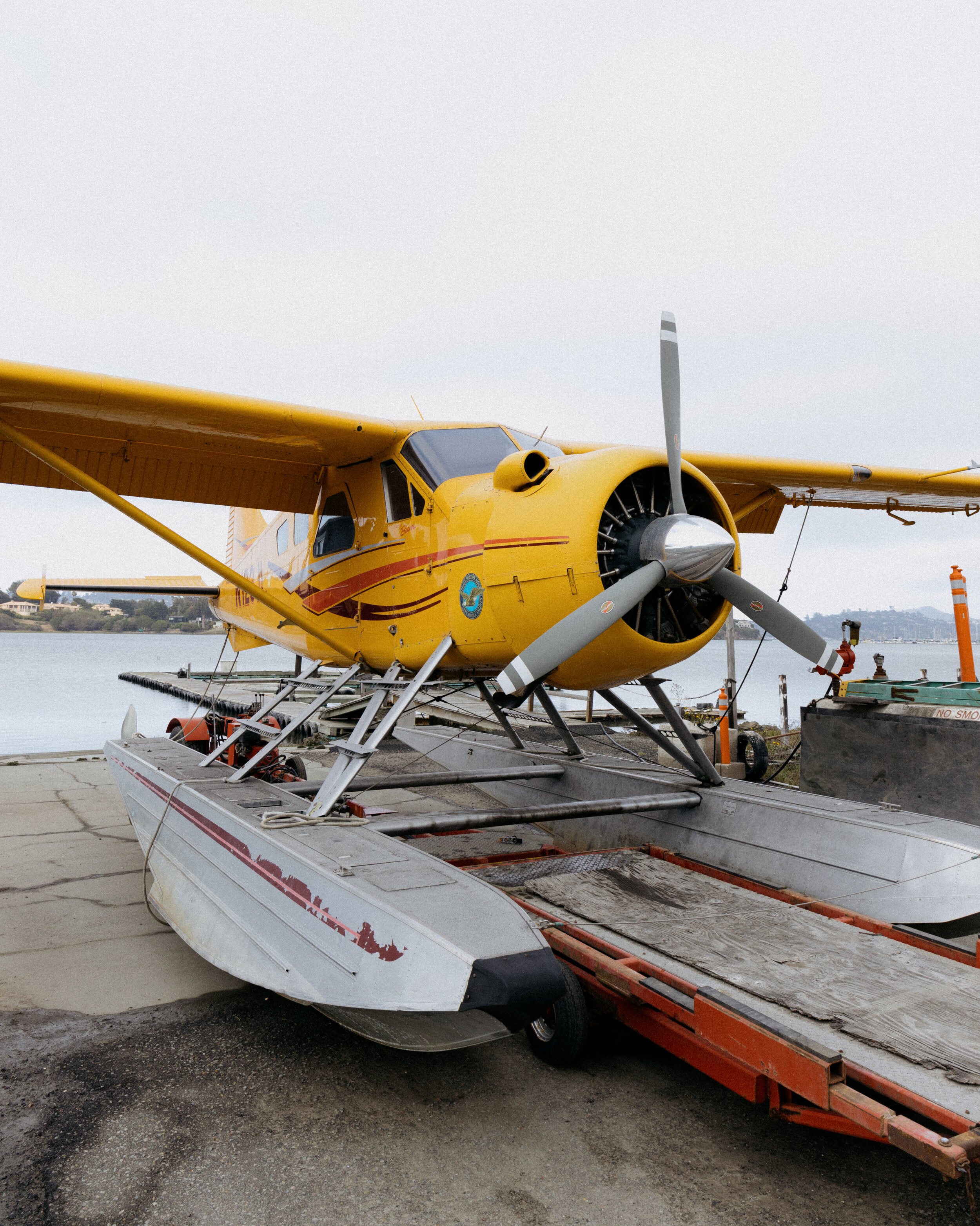 Yellow seaplane on a floating dock near the water, with a propeller and pontoons.