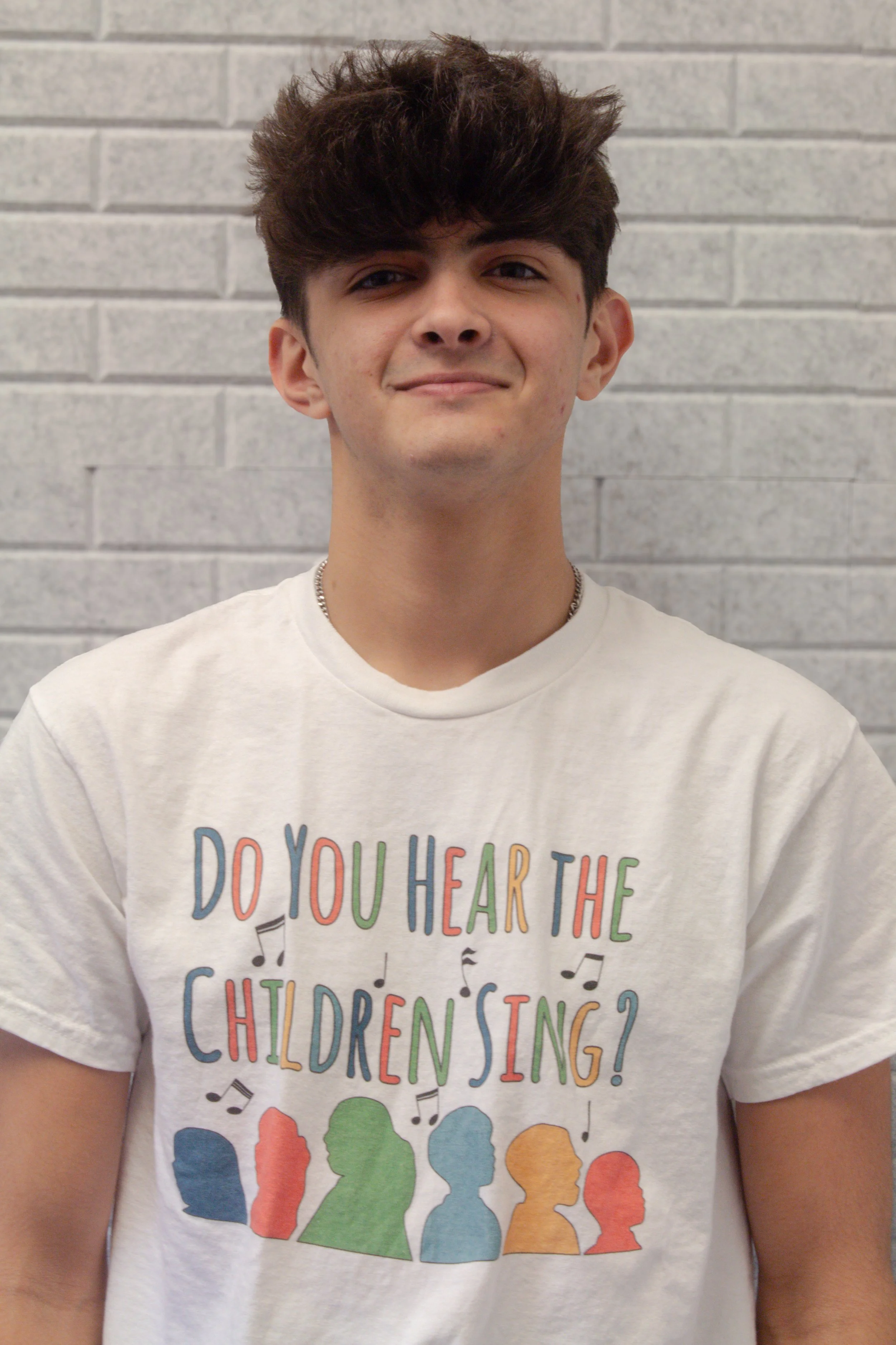 A person wearing a white T-shirt with the text 'Do you hear the children sing?' and colorful silhouettes of children's faces.