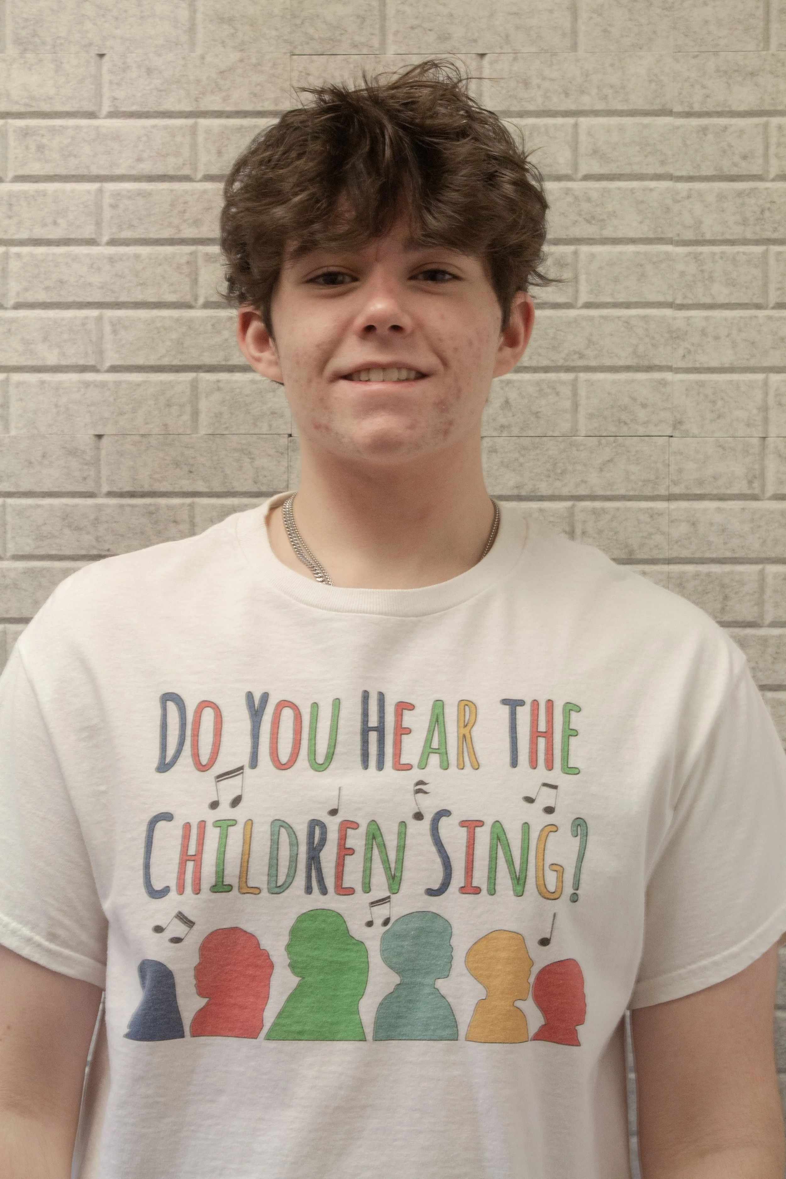 A person wearing a white T-shirt with colorful text and silhouettes of heads in rainbow colors, set against a brick wall background.