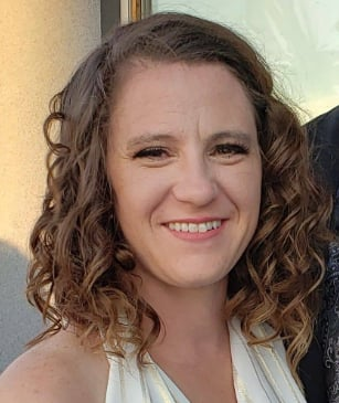 Pictured is Erin with her hair in curls and formal makeup. She is wearing a white halter top dress. She has brown eyes and dark blonde hair that is almost brown.