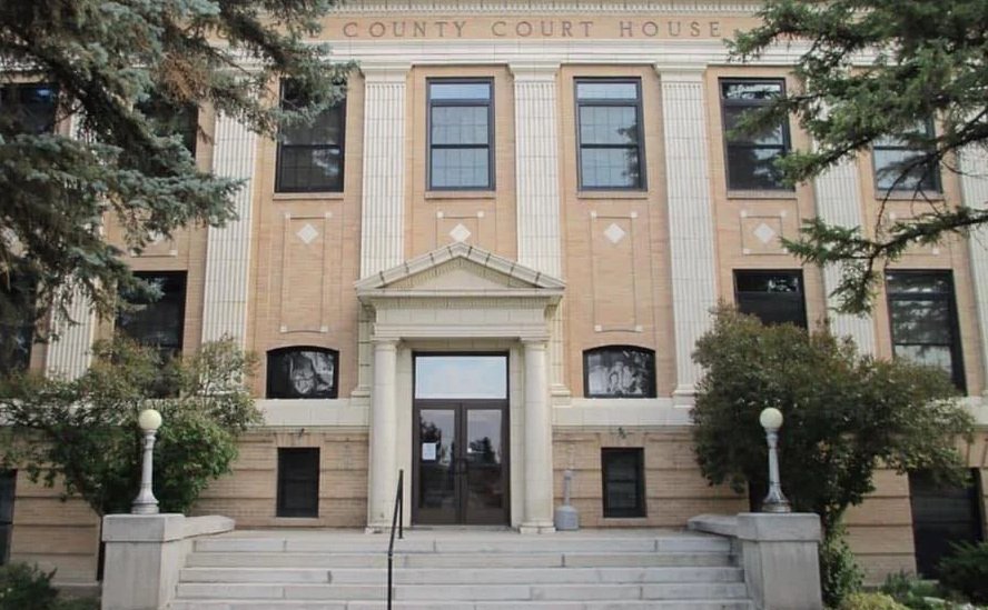 A brick county courthouse building with steps leading to the entrance, flanked by trees and decorative lamps, with the words " Powell County Courthouse" at the top.