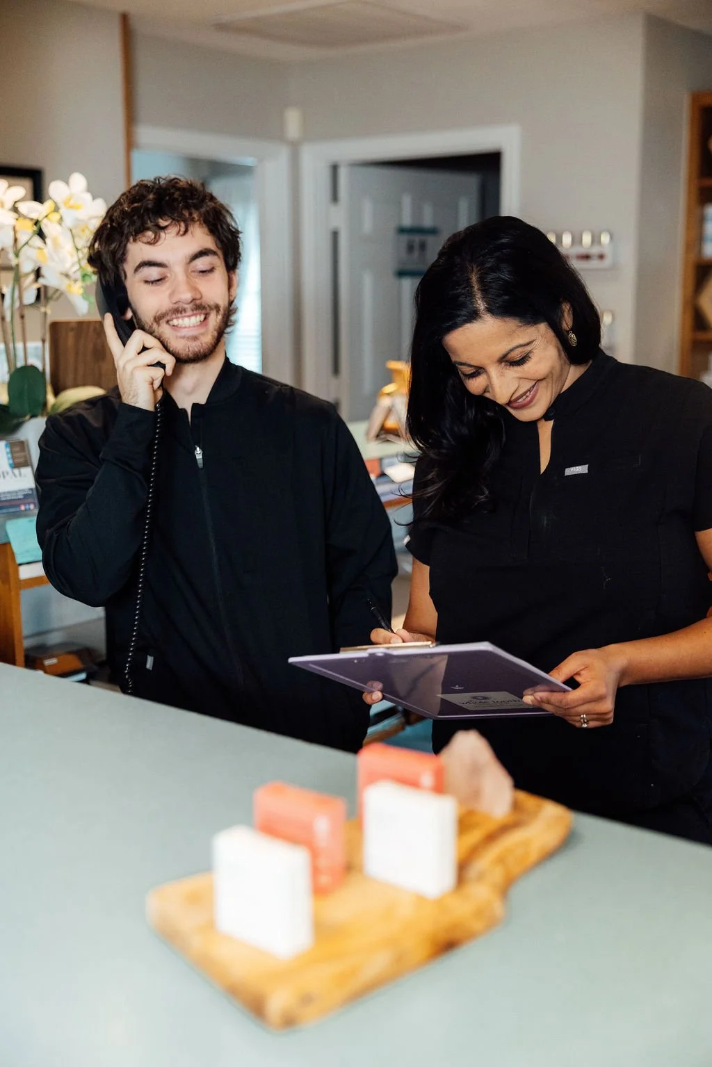 Dr. Genz and Sonny, our Patient Experience Coordinator chatting at the reception desk, while answering a phone call, all smiles.