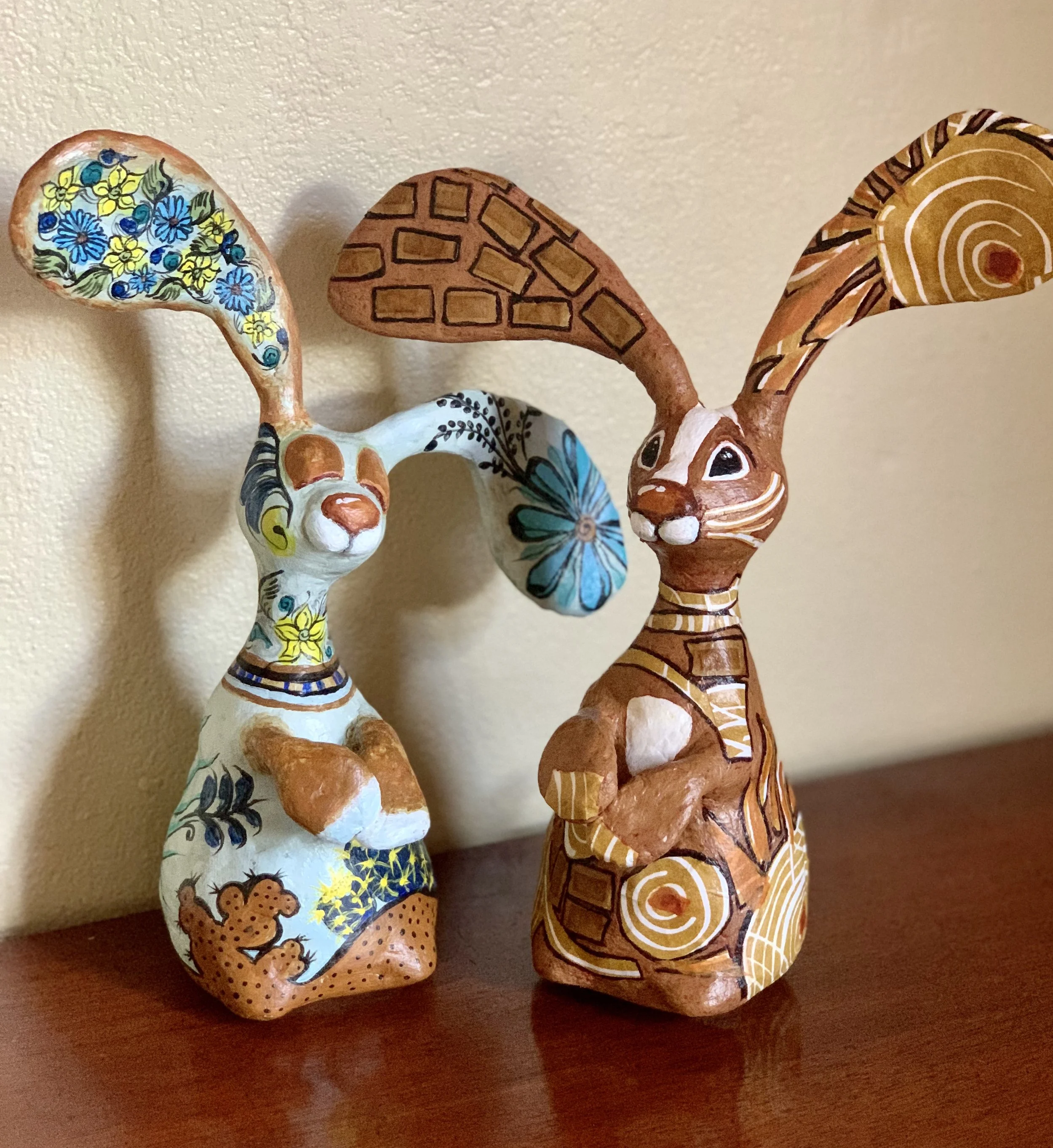 Decorative ceramic rabbit figurines with painted colorful patterns and floral designs, placed on a wooden surface against a beige wall.