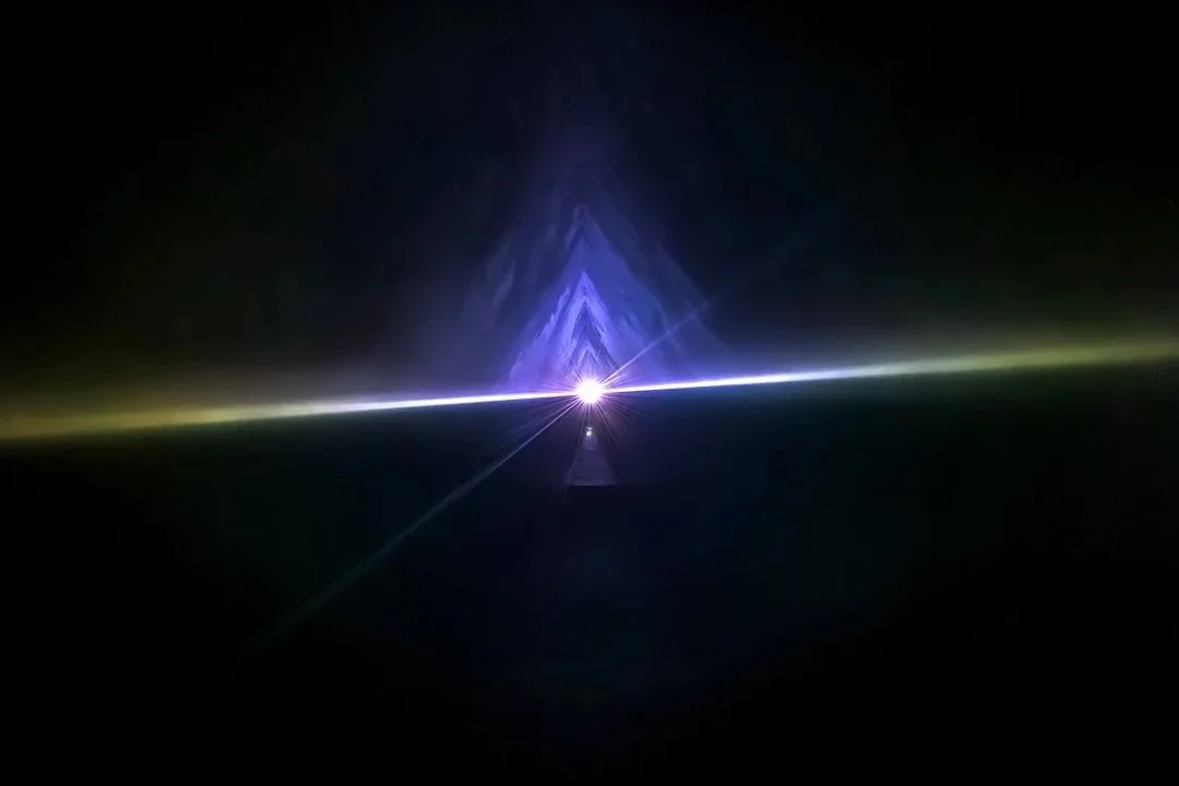 A laser light show with symmetric blue and white laser beams forming a triangular pattern in dark space.