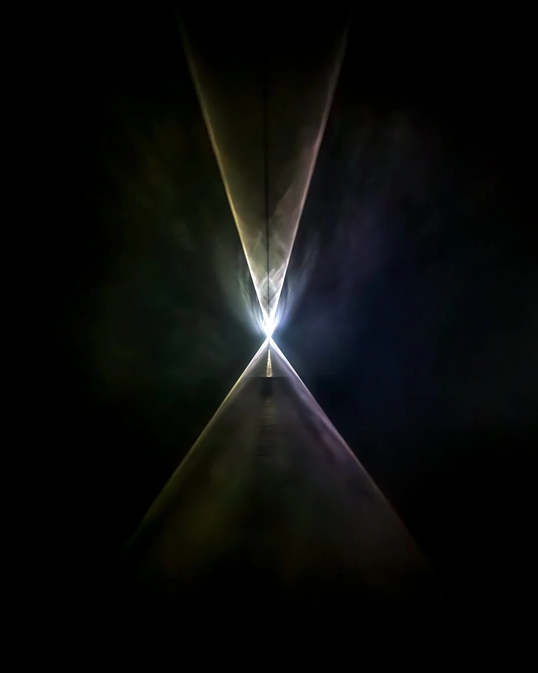 Bright light at the end of a reflective tunnel creates symmetrical light beams in a dark space.