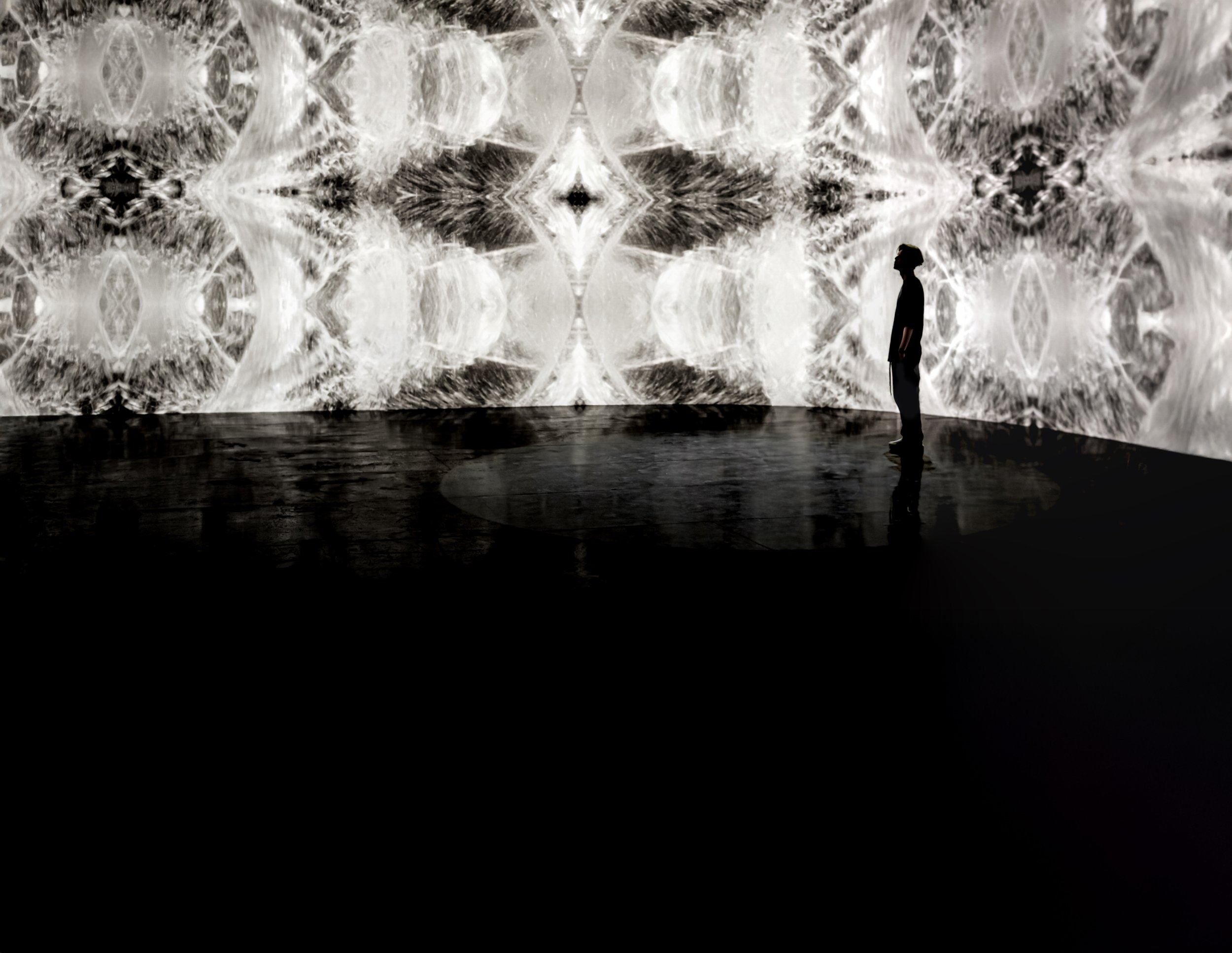 A person standing in front of a large digital wall displaying swirling black and white abstract patterns.