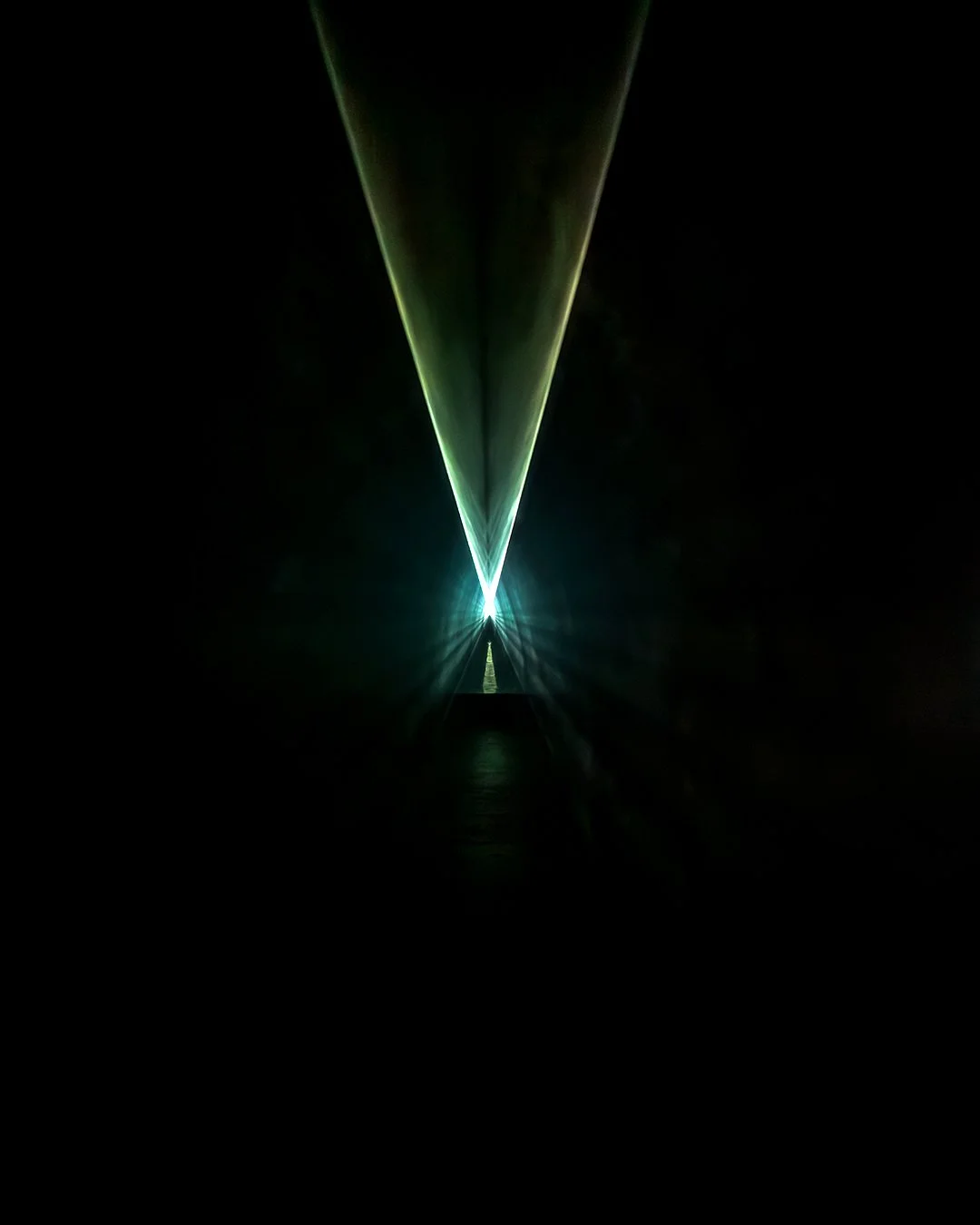 Green laser beam creating a V-shape in a dark tunnel.
