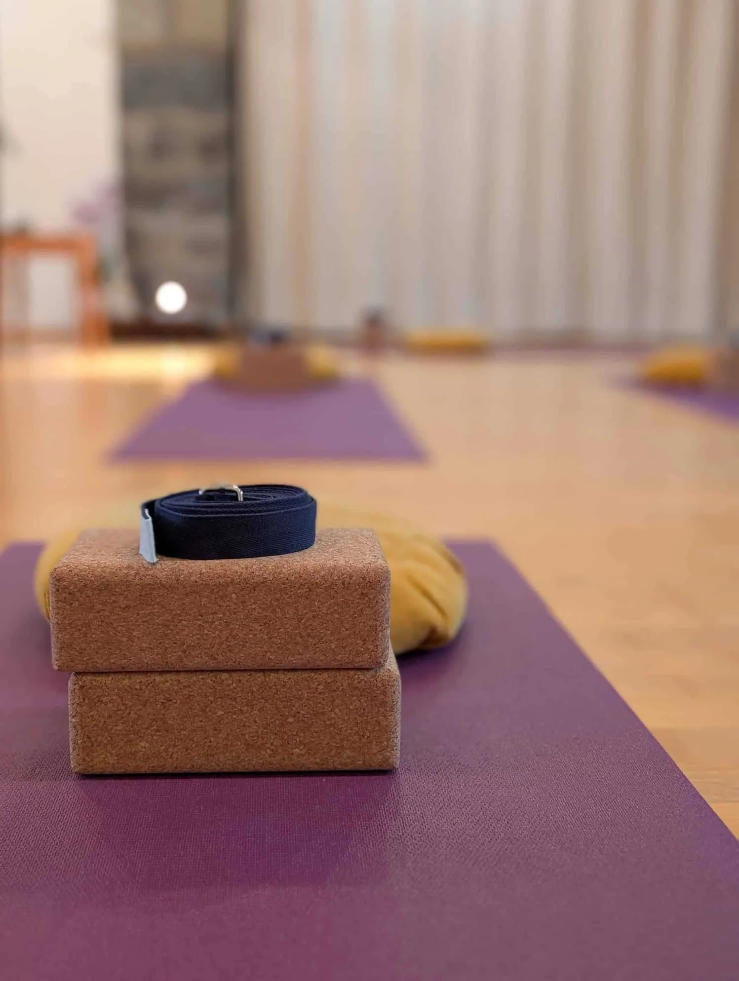 Yoga mats, bolsters, and blocks arranged in a meditation or yoga room with a blanket and a belt on the blocks.