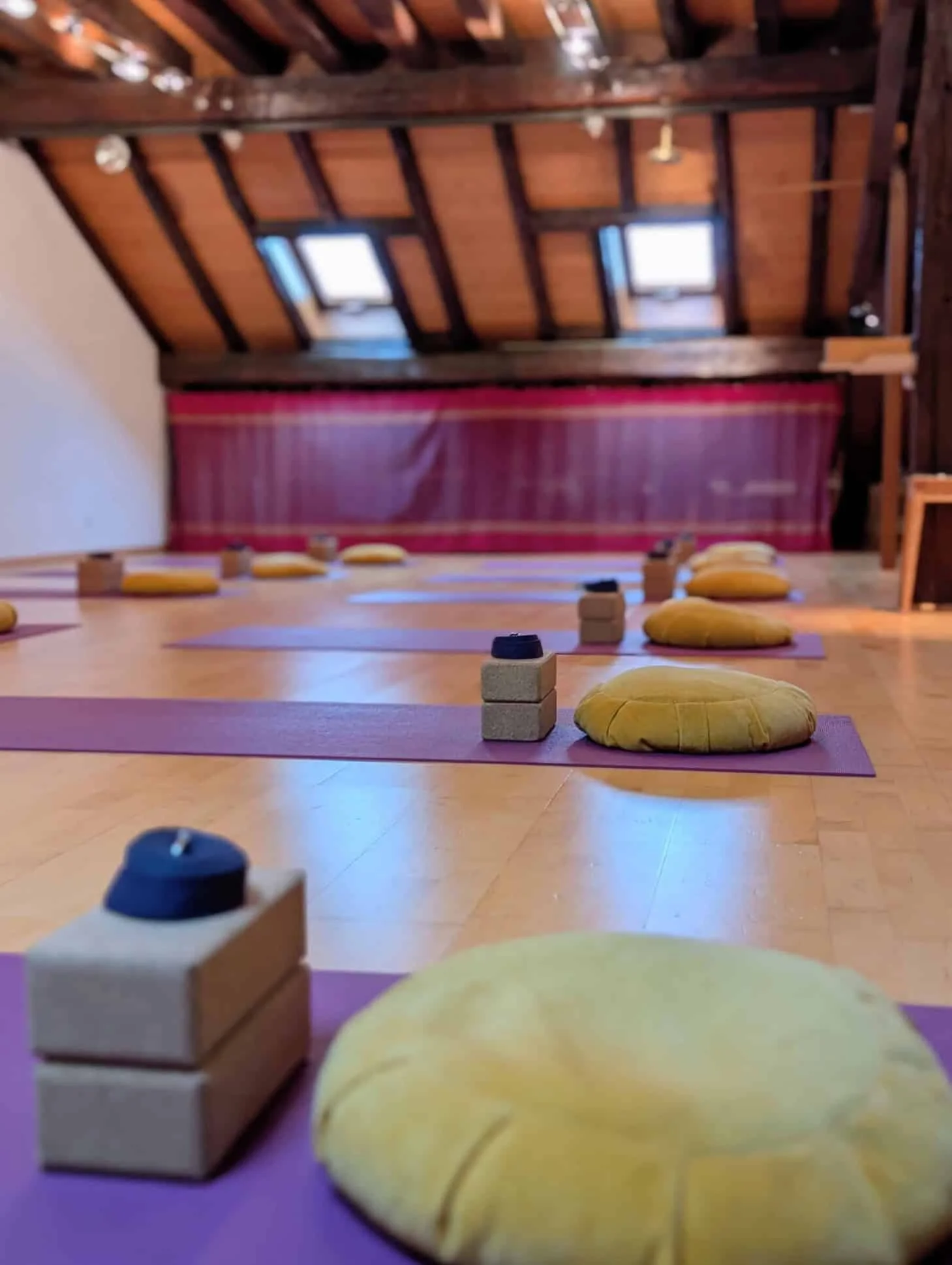 Yoga mats, cushions, and blocks set up in a peaceful wooden attic space with skylights.