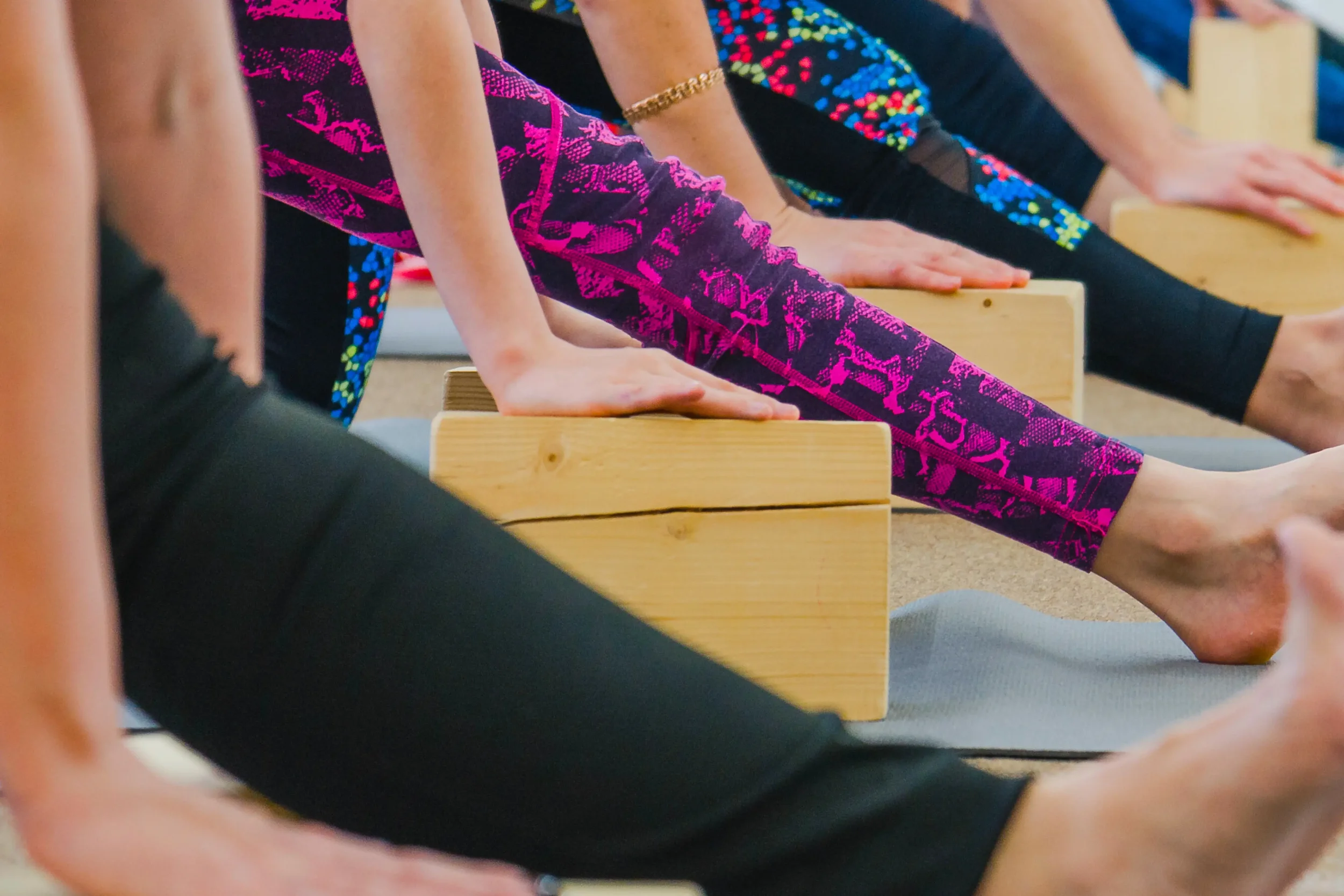 People practicing yoga on yoga mats, stretching with hands on wooden yoga blocks.