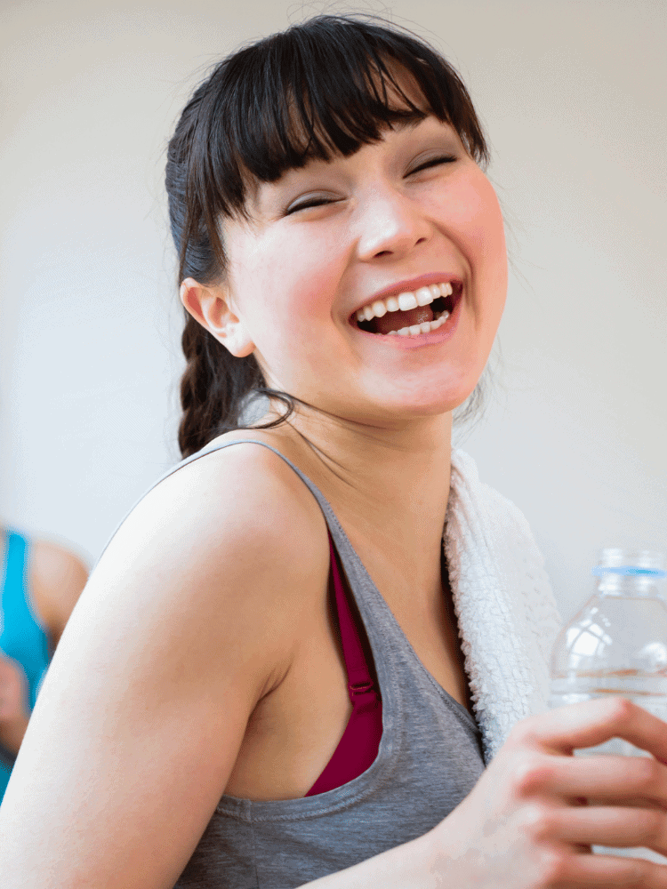 Young woman in workout clothes laughing and holding a water bottle.