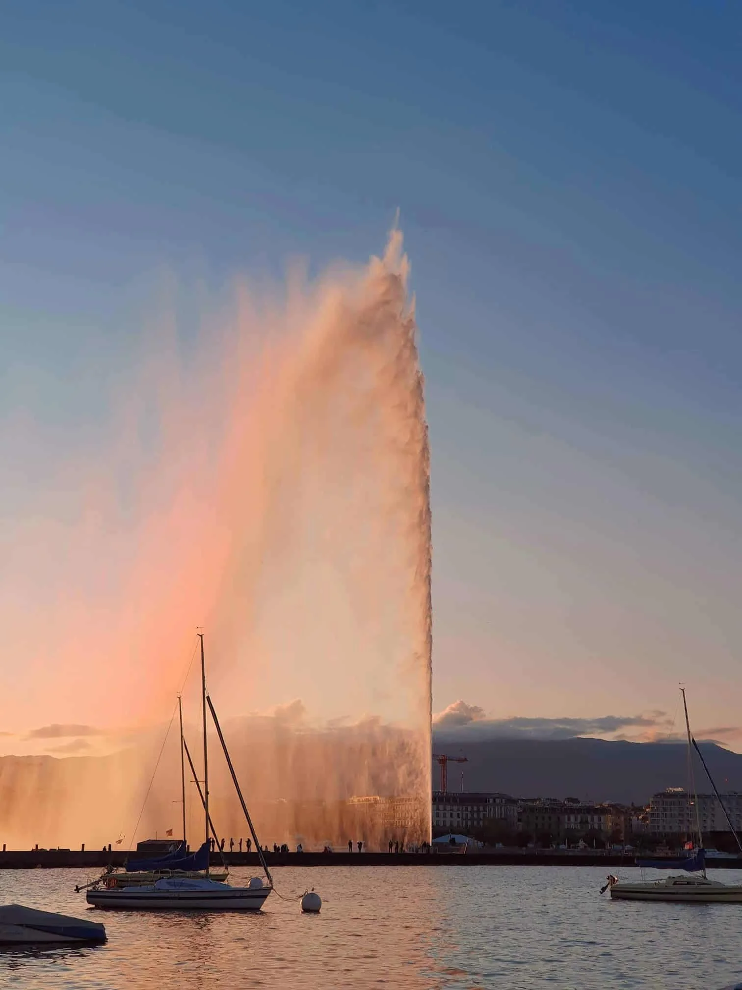 Jet d'eau in Geneva spraying water high into the sky near boats in a harbor during sunset.