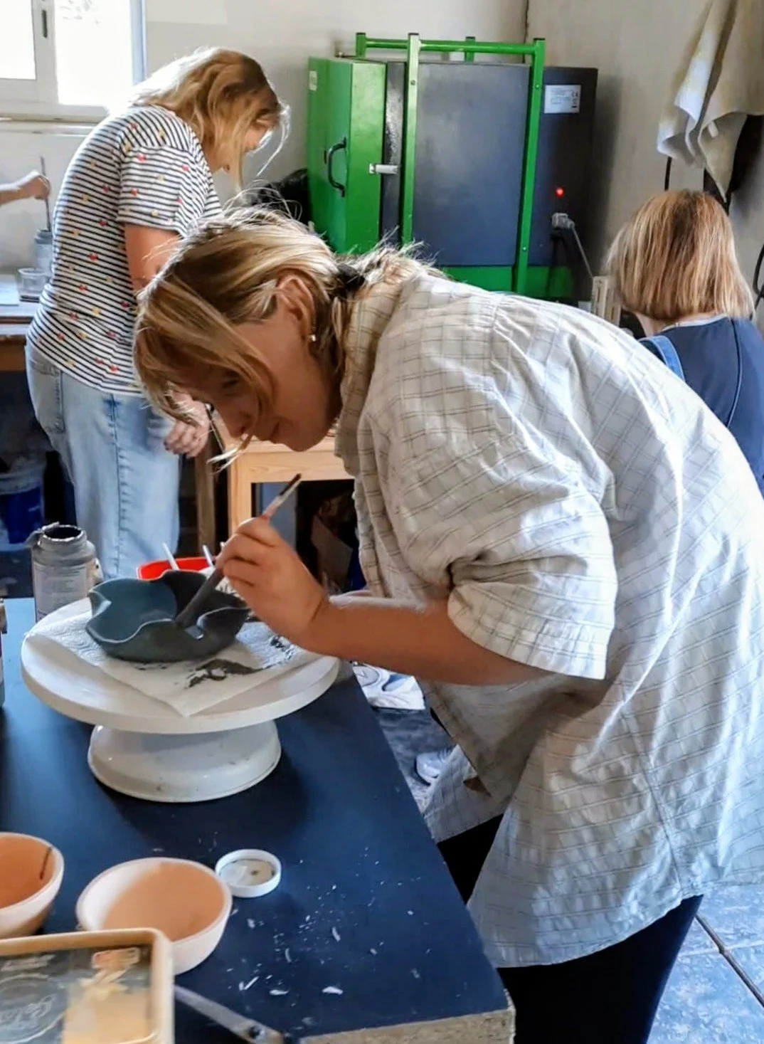 People working on pottery at a pottery studio, with a person painting a pottery piece.