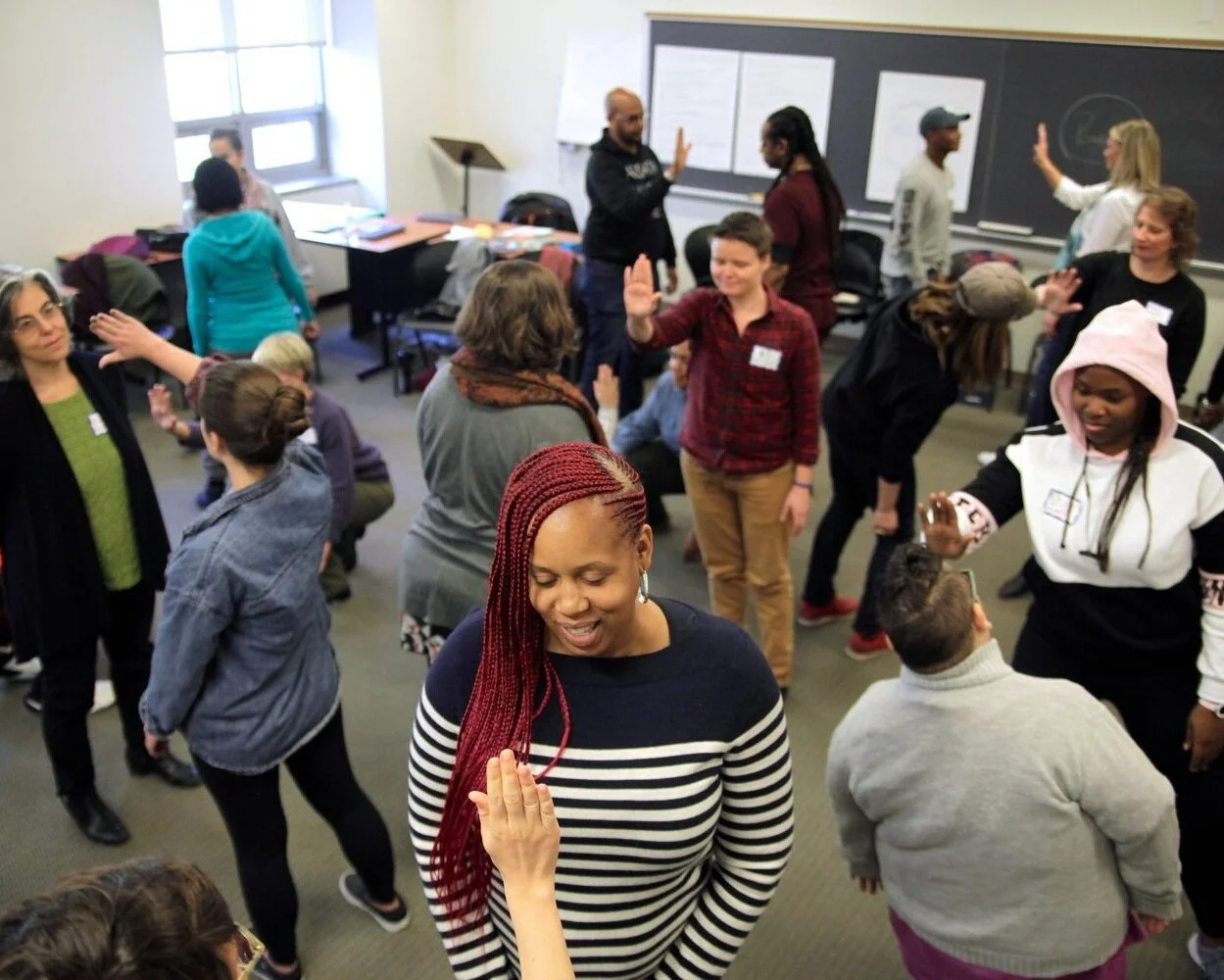 A diverse group of people in a classroom participating in a theatre game