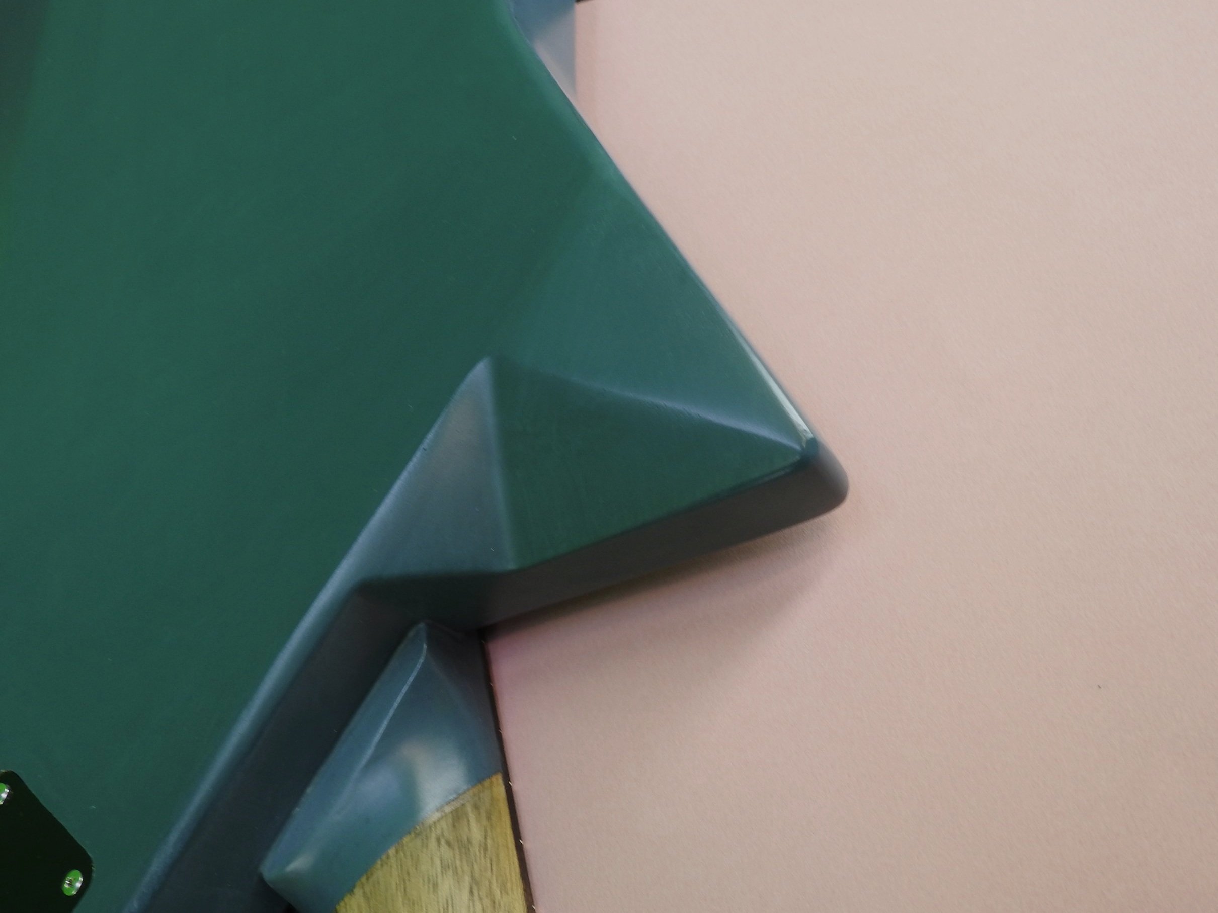 Close-up of a guitars upper bout resting on a pale pink surface.