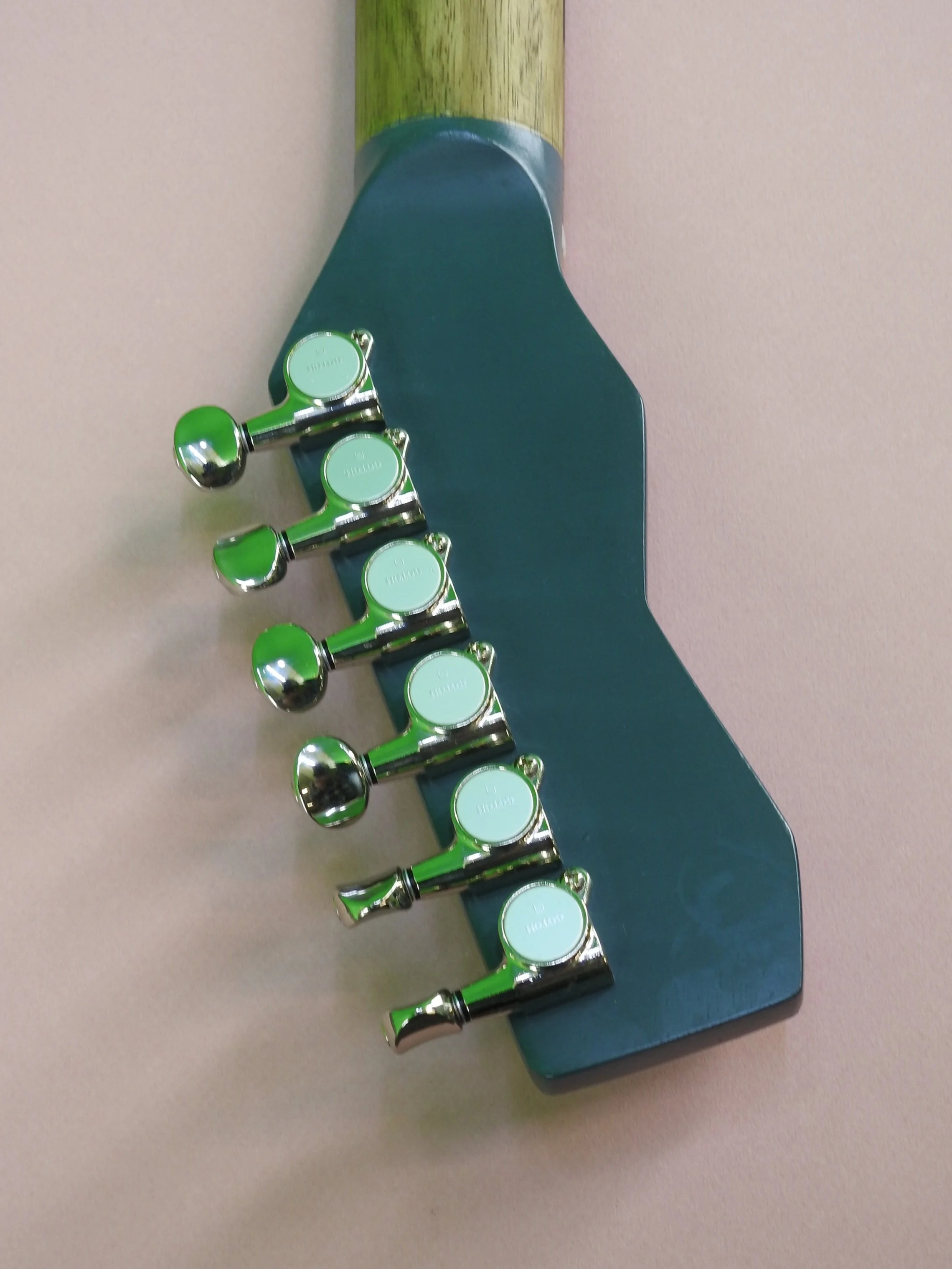 A row of six shiny silver tuning pegs on a blue guitar headstock.