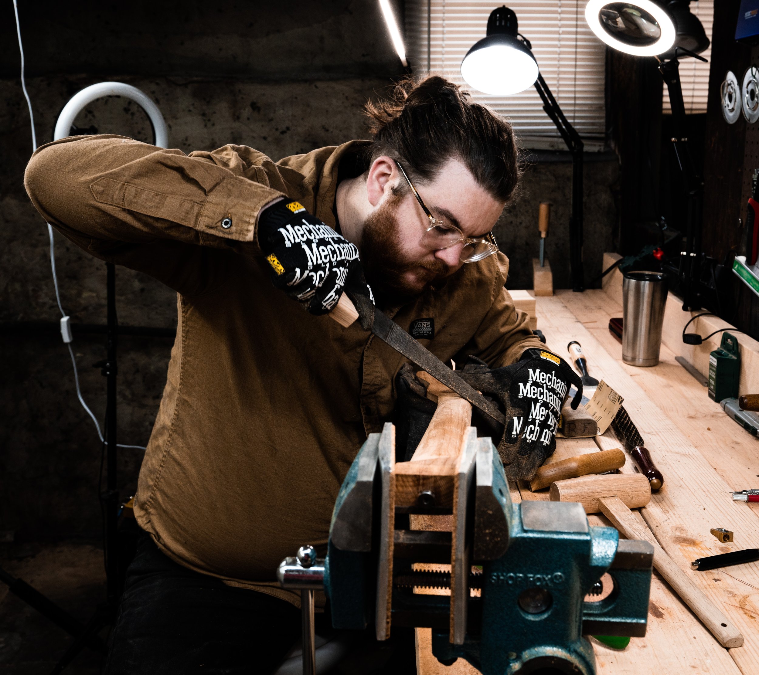 A man working on a woodworking project in a workshop, using a handsaw on a piece of wood secured in a vise.