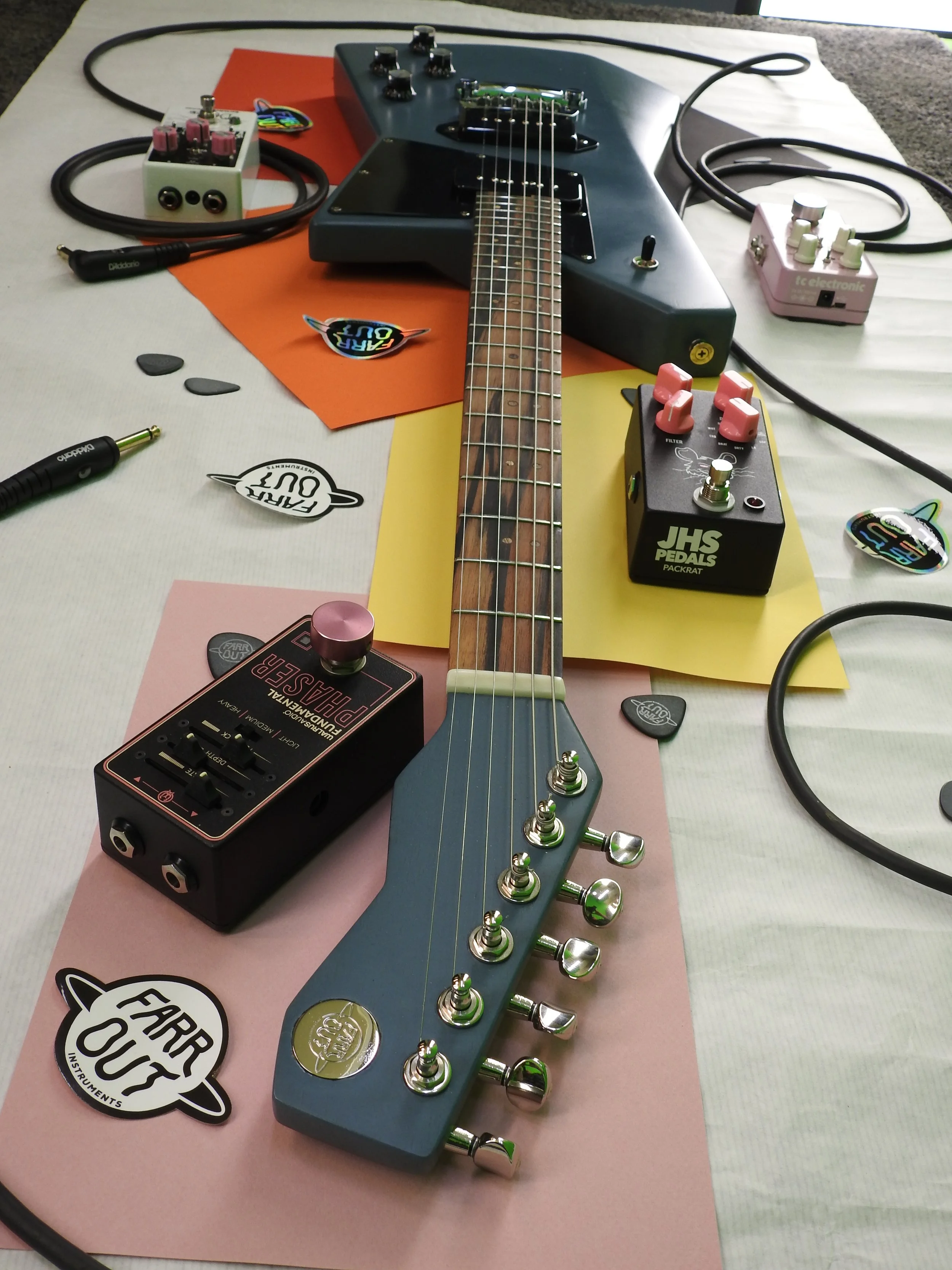 Electric guitar surrounded by various guitar pedals on a table covered with paper stickers and foam mats.