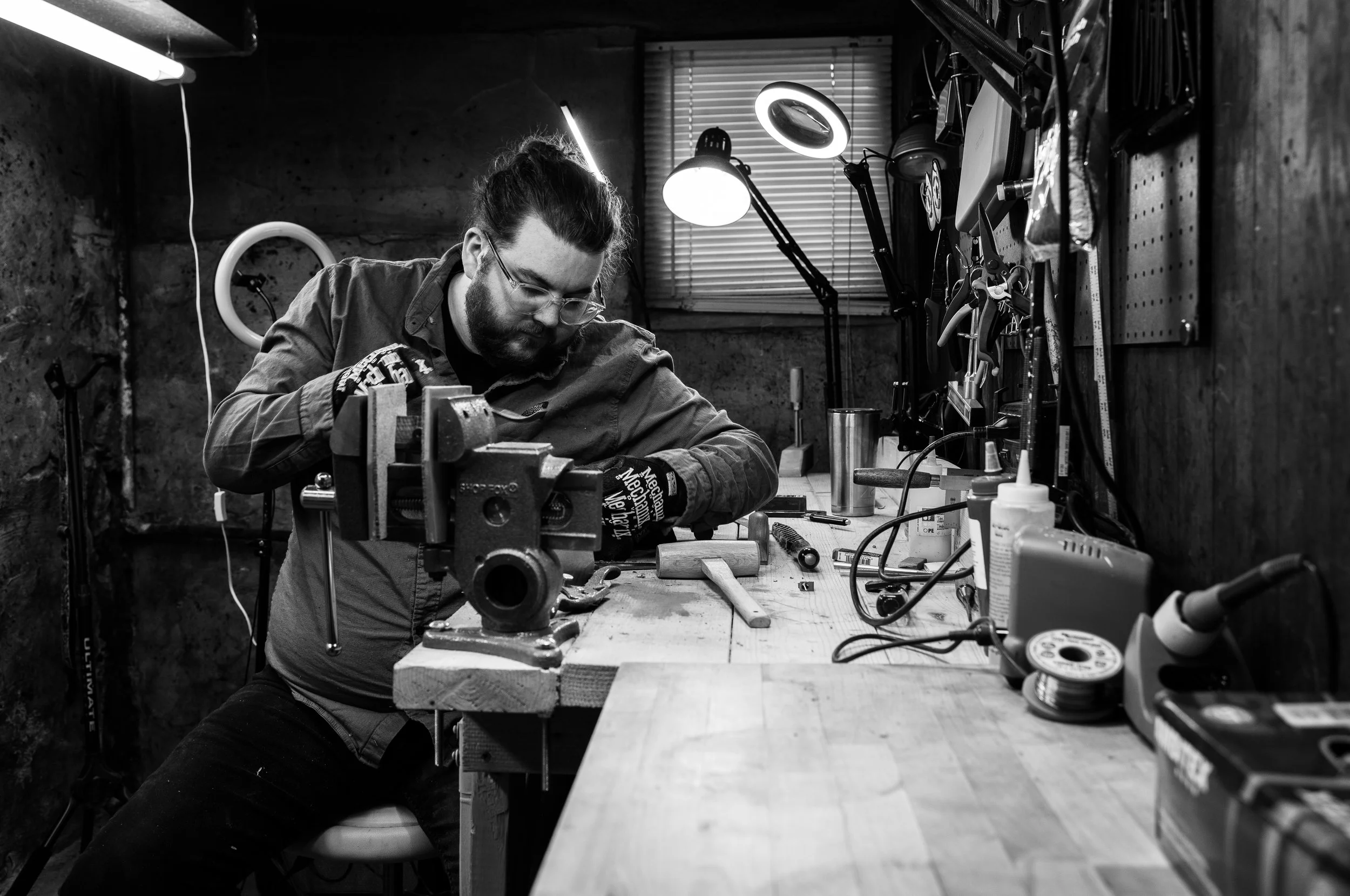 Man working on a project at a workbench in a workshop, surrounded by tools and equipment.