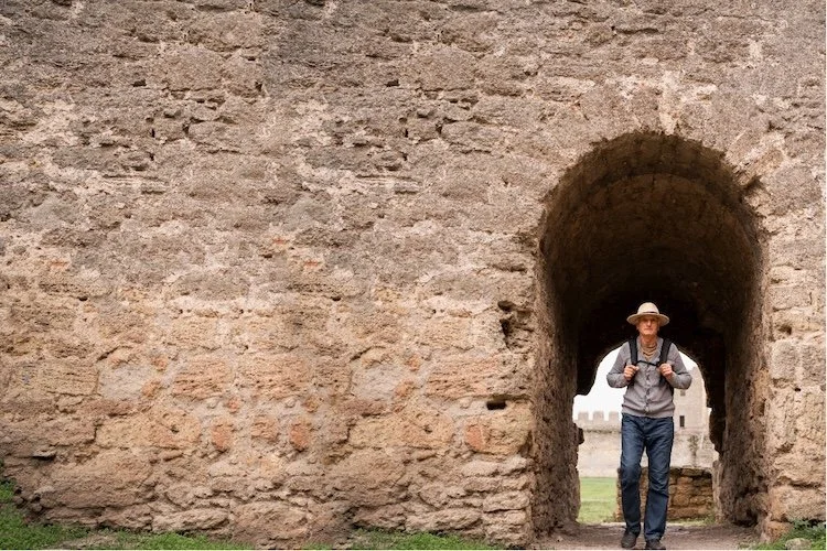 old man walking through a medieval stone wall
