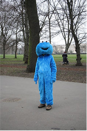 man dressed up as a blue monster stands in a park
