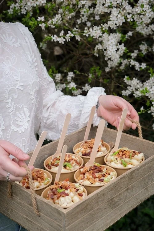 Waitress holding a wooden crate of street food; mac and cheese with delicious toppings