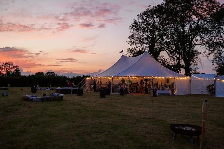 Wild Fork's wedding marquee package combining a tent, field and catering. The tent has beautiful festoon lighting and hay bales outside.