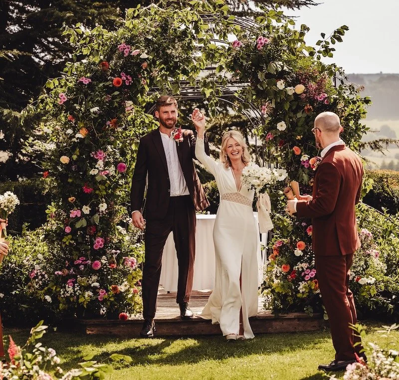 A bohemian style couple getting married under an arch at North Cadbury Court