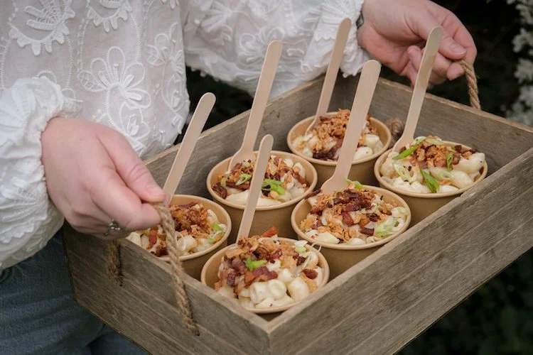 Wild Fork's team carrying a wooden box of mac & cheese in takeaway containers with various toppings