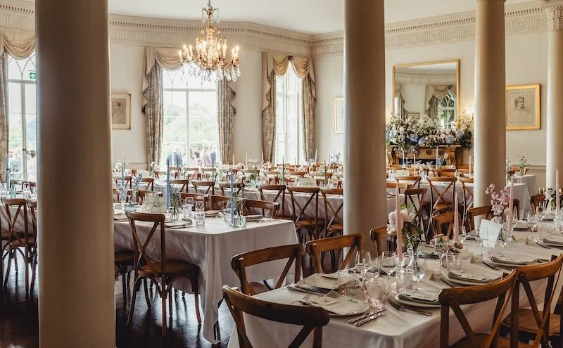 Inside a beautiful country house wedding venue, with long tables and taper candles