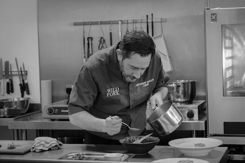 Black and white photo of a chef plating a fish dish