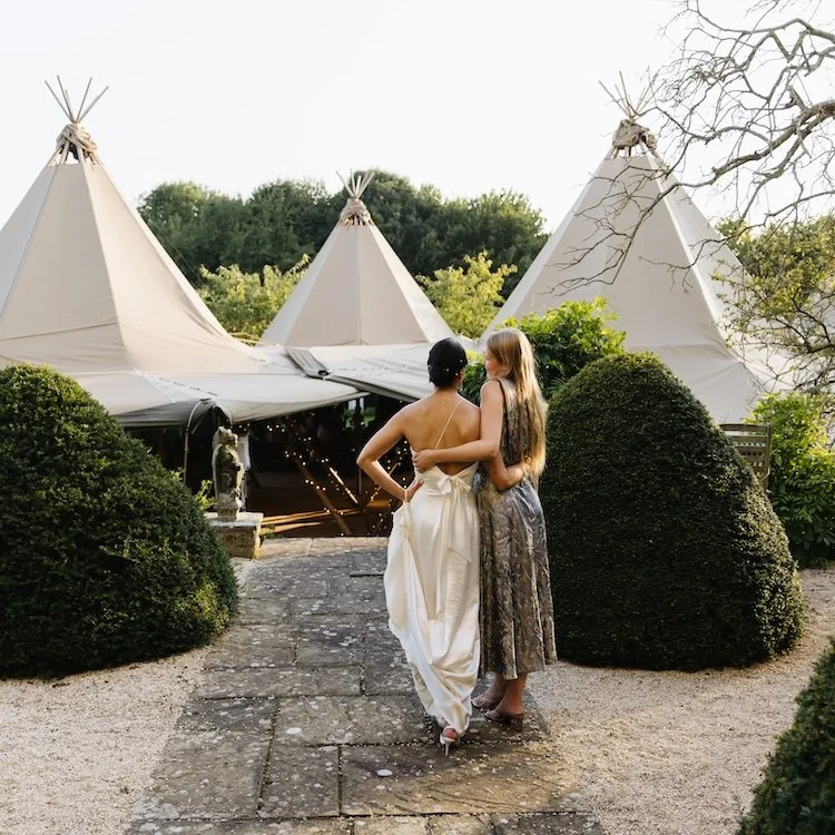 A bride and her bridesmaid overlooking a beautiful tipi wedding set up