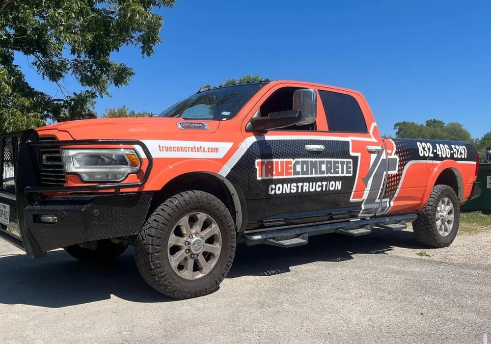 Orange and black construction pickup truck with "True Concrete Construction" branding parked on a sunny day.