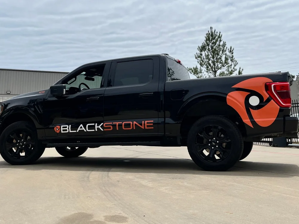 Black pickup truck with "Blackstone" logo parked in front of a building with overcast sky.