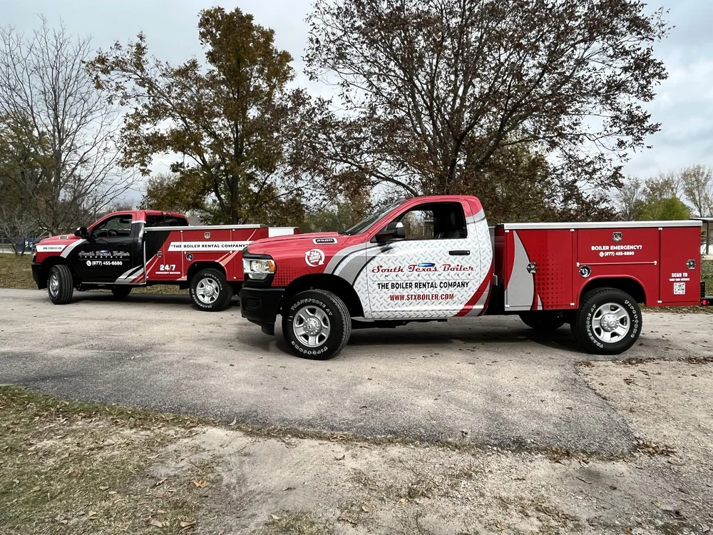 Two red and white trucks with "South Texas Boiler" branding parked outdoors on a paved surface near trees.